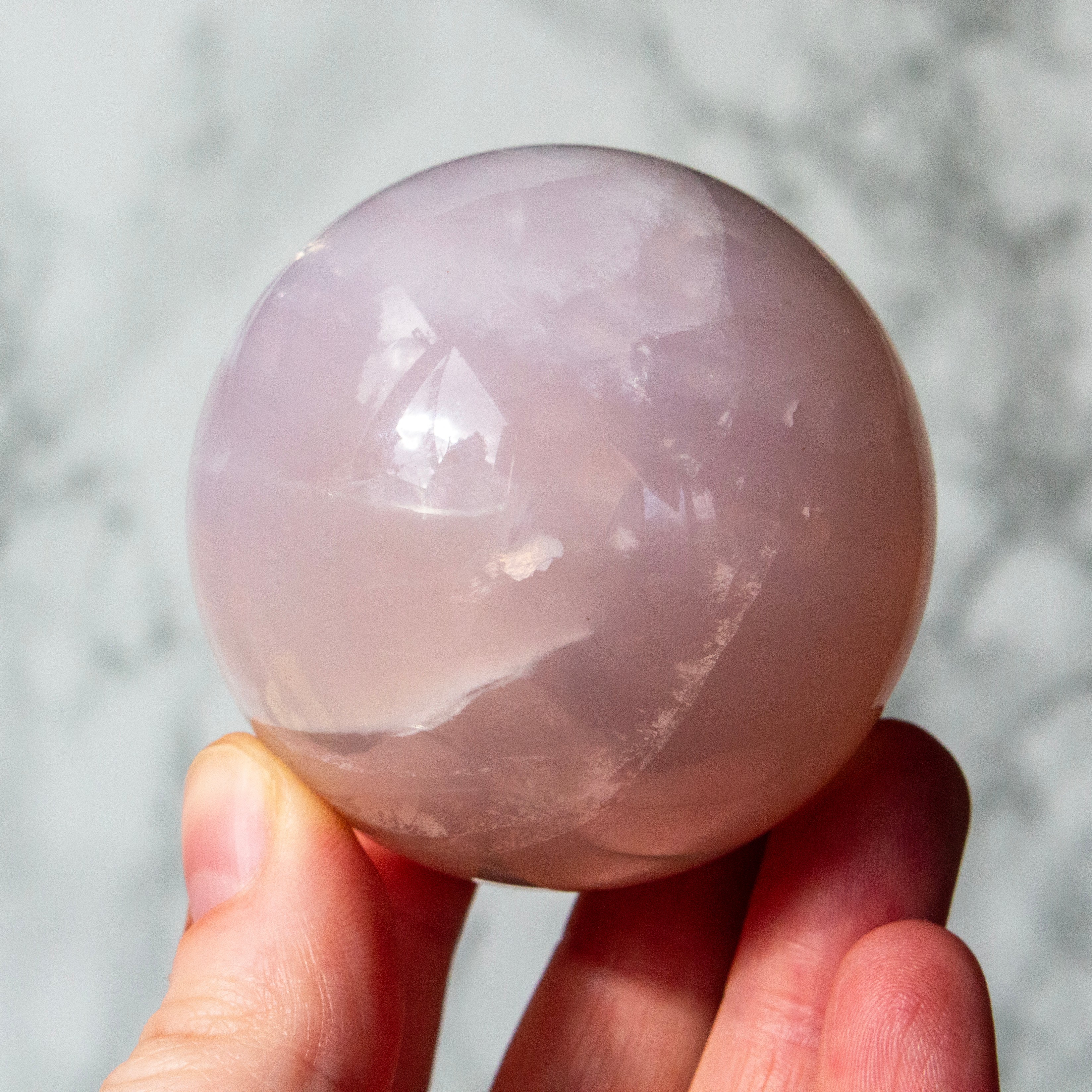 Hand holding a pink crystal ball against a neutral background