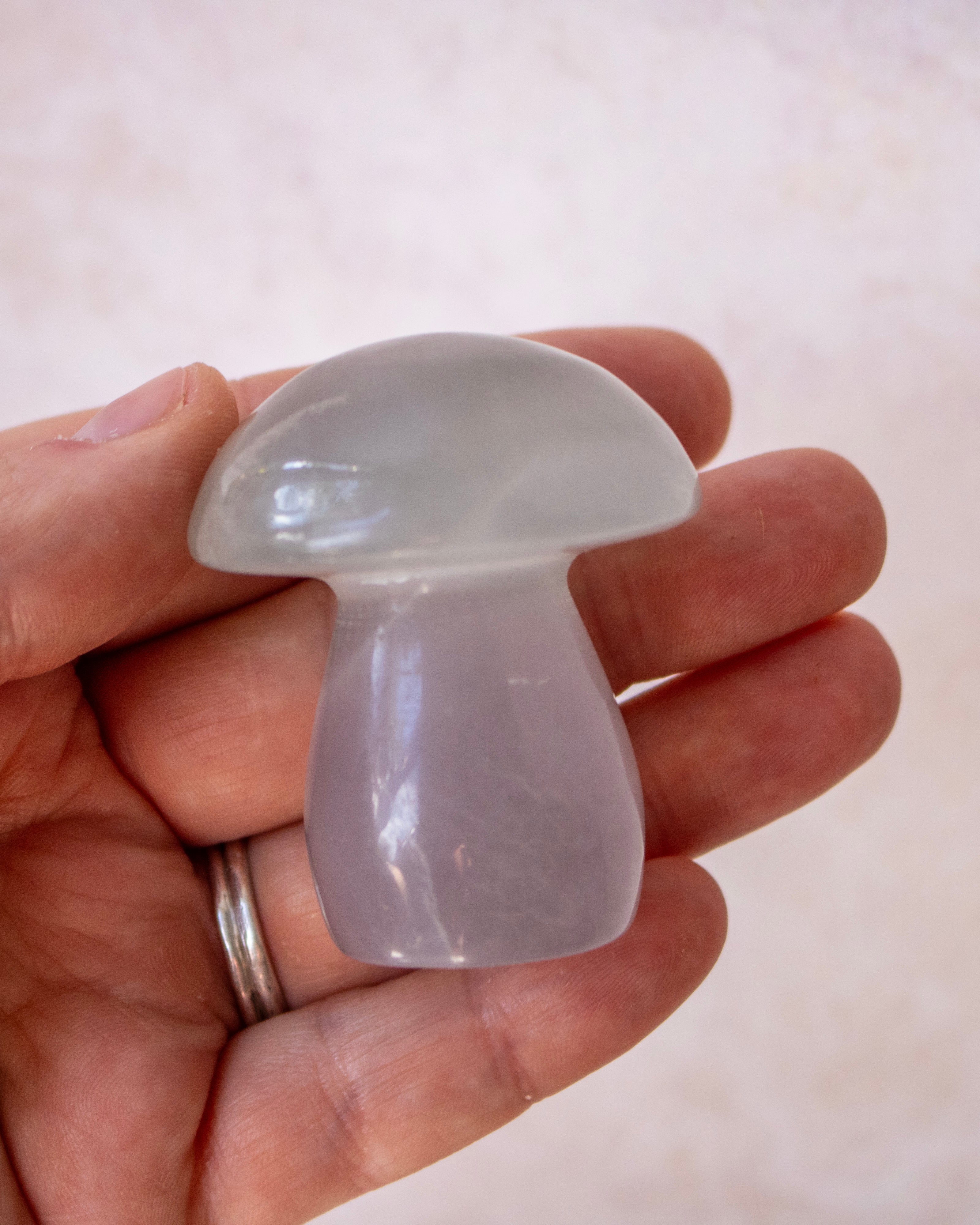 A hand holding a small mushroom-shaped translucent stone ornament, likely fluorite, against a soft beige background.