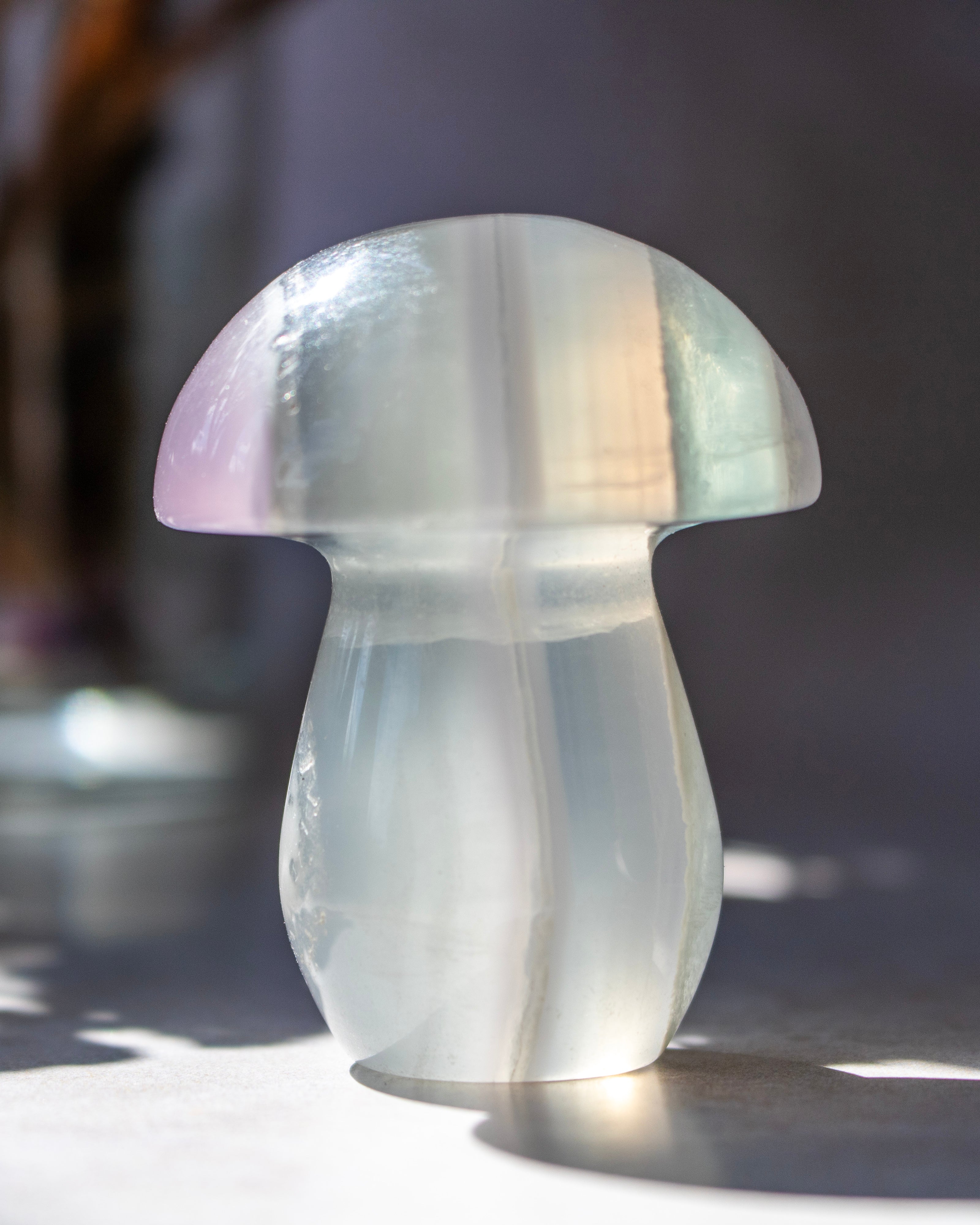 A mushroom-shaped translucent crystal sculpture with a smooth, polished finish, shown in soft natural light on a neutral surface.
