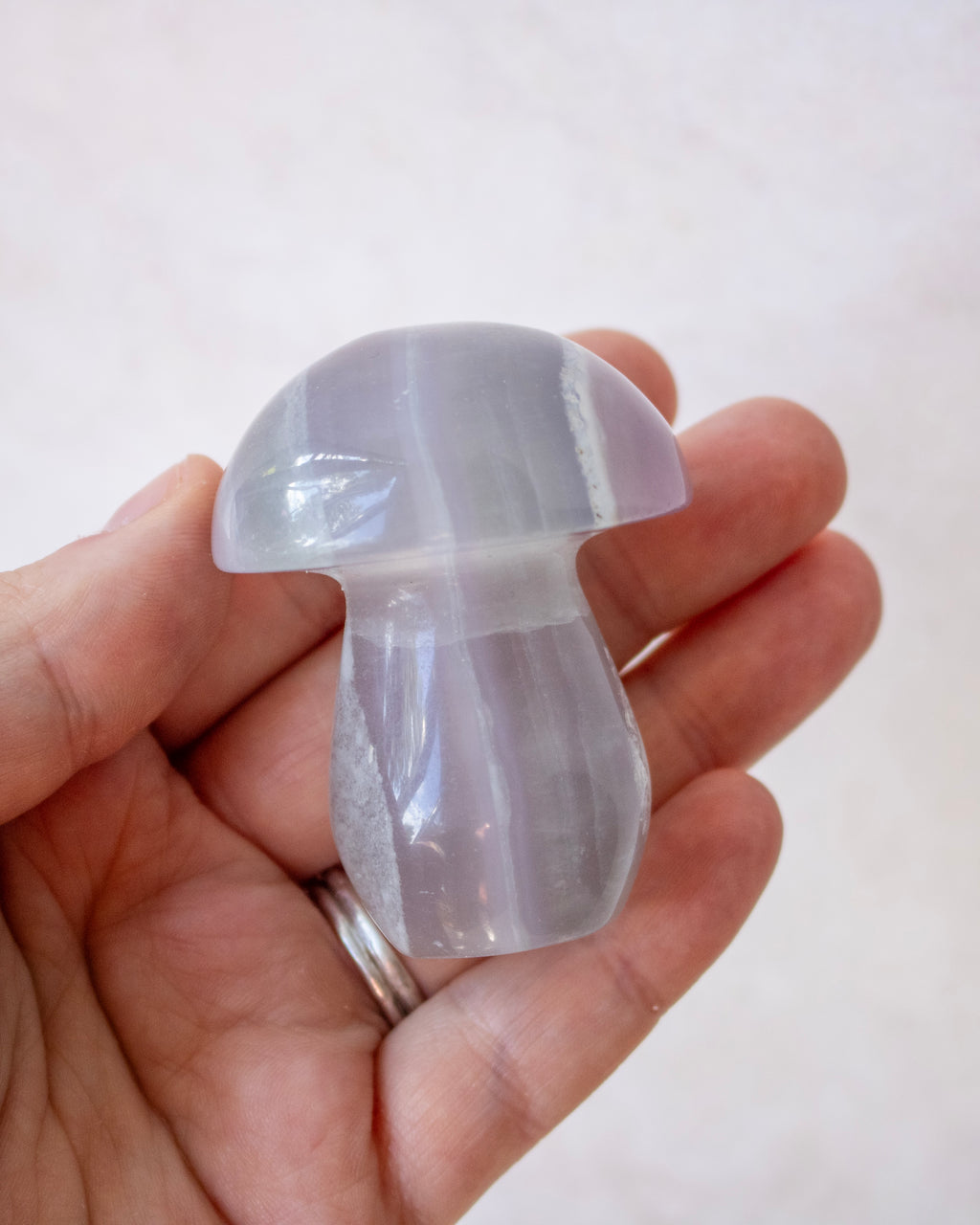 A hand holding a small, mushroom-shaped translucent stone with a smooth, polished surface and subtle banding.