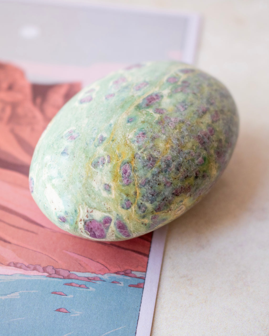 A polished green stone with purple and yellow marbling, resting on a printed card against a light neutral background.