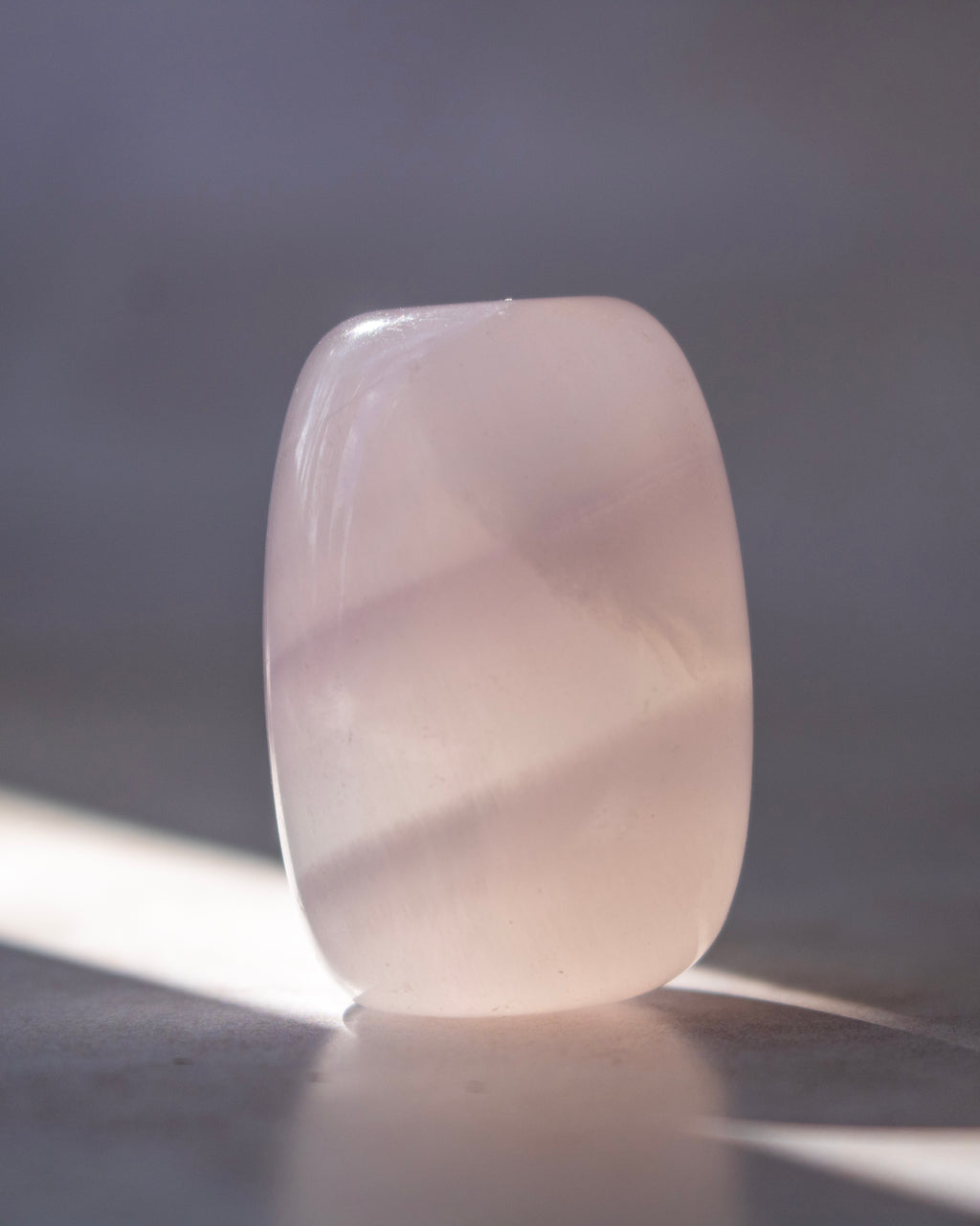 A smooth, rounded rectangular stone or glass block with a pale pinkish-white translucent color, standing upright on a surface with soft shadows and light.