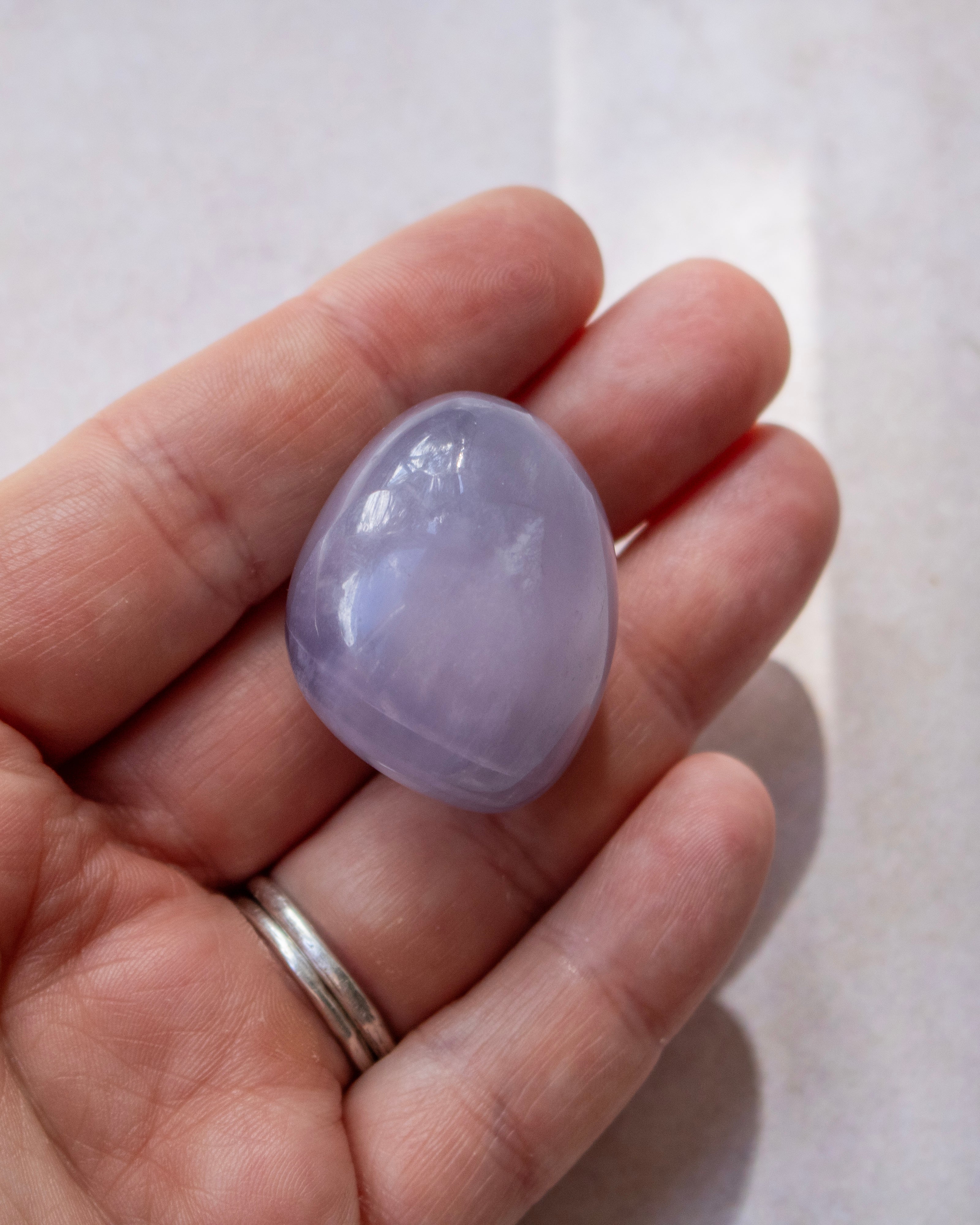 A smooth, polished light purple tumbled stone, likely a amethyst, resting on the palm of a hand.
