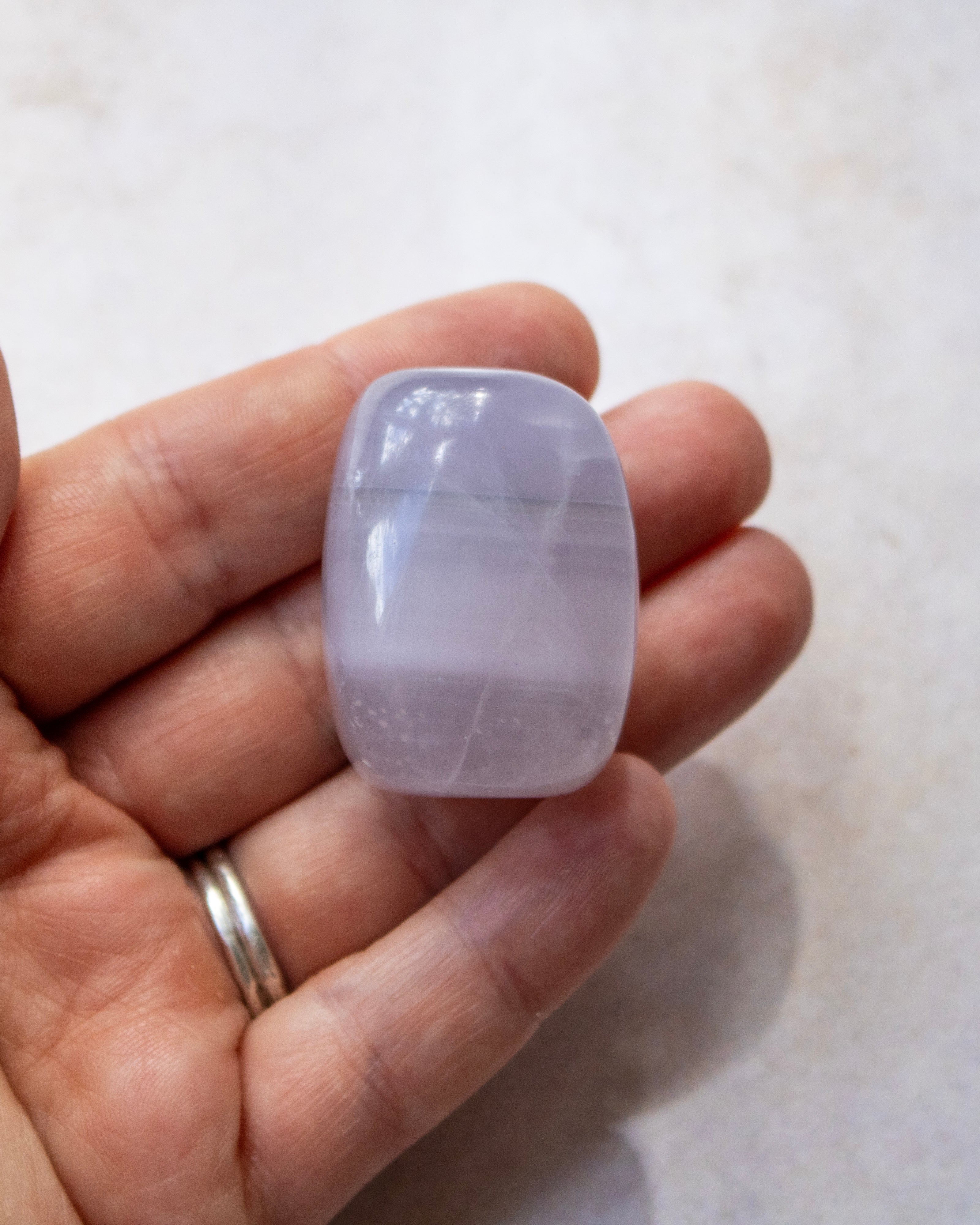 A polished light purple stone, held in a person's hand against a light beige background.
