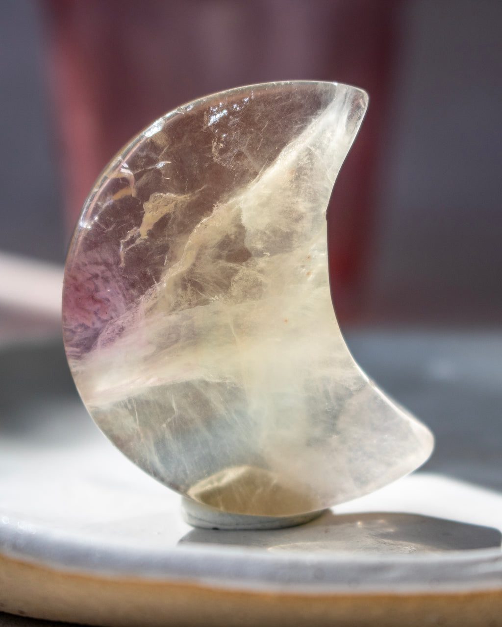 A crescent-shaped clear crystal stone with natural inclusions, displayed on a small stand on a ceramic surface.