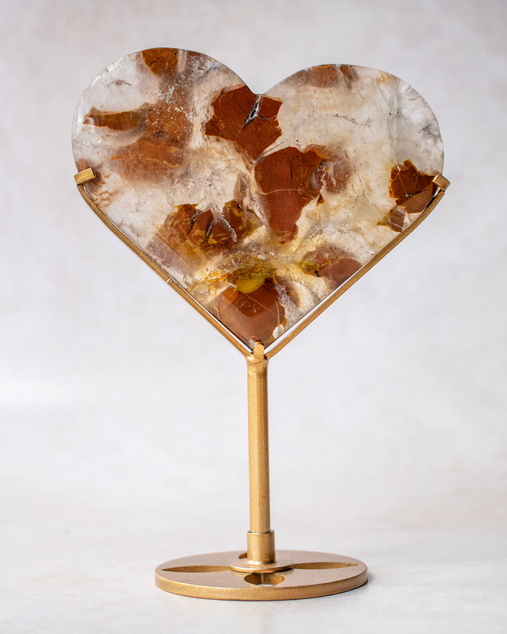 A heart-shaped stone with embedded brown elements, mounted on a polished gold-toned metal stand with a round base.