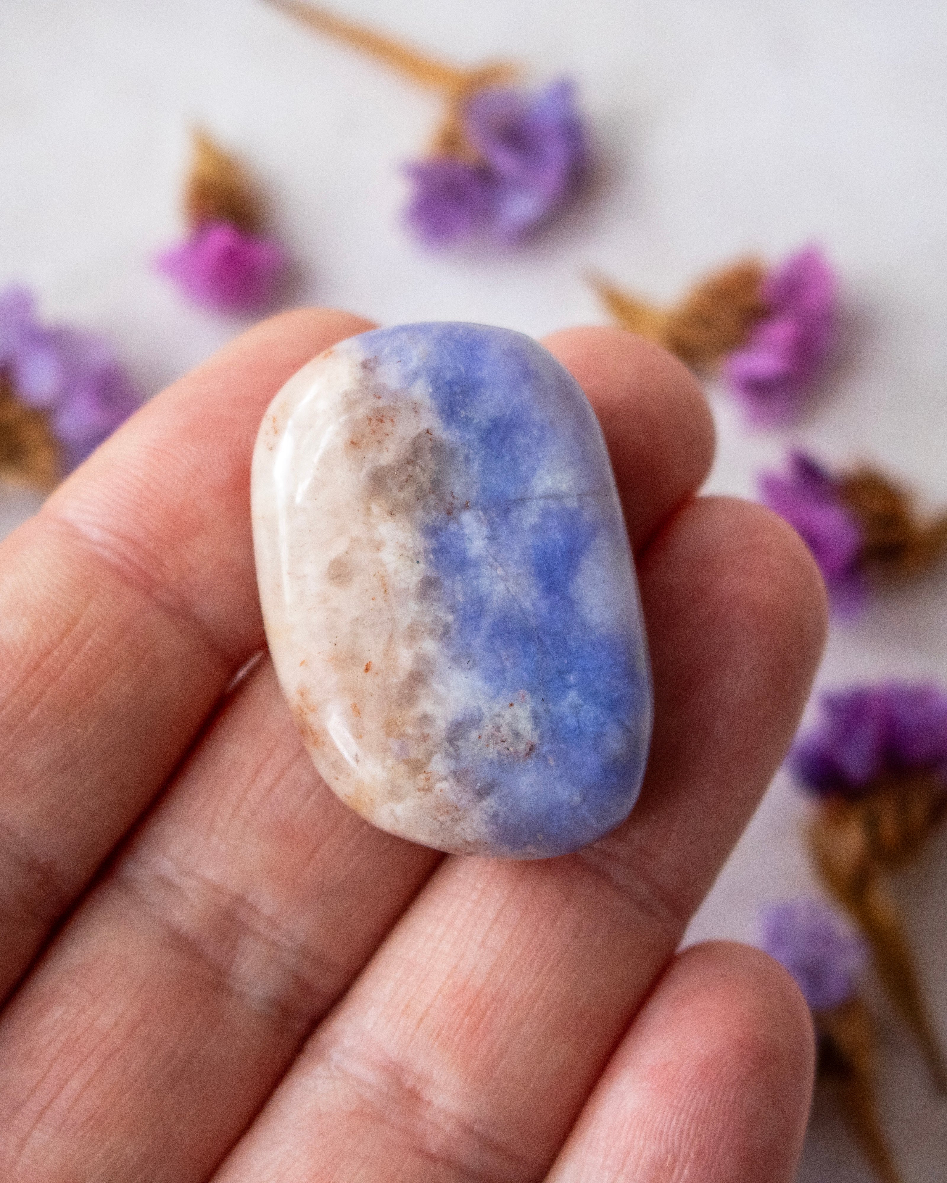 A polished tumbled stone with a split blue and beige coloration being held in someone's hand