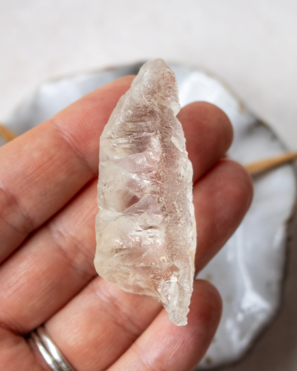 A raw, rough translucent crystal stone held in a person's hand, showing its natural jagged edges and internal inclusions.