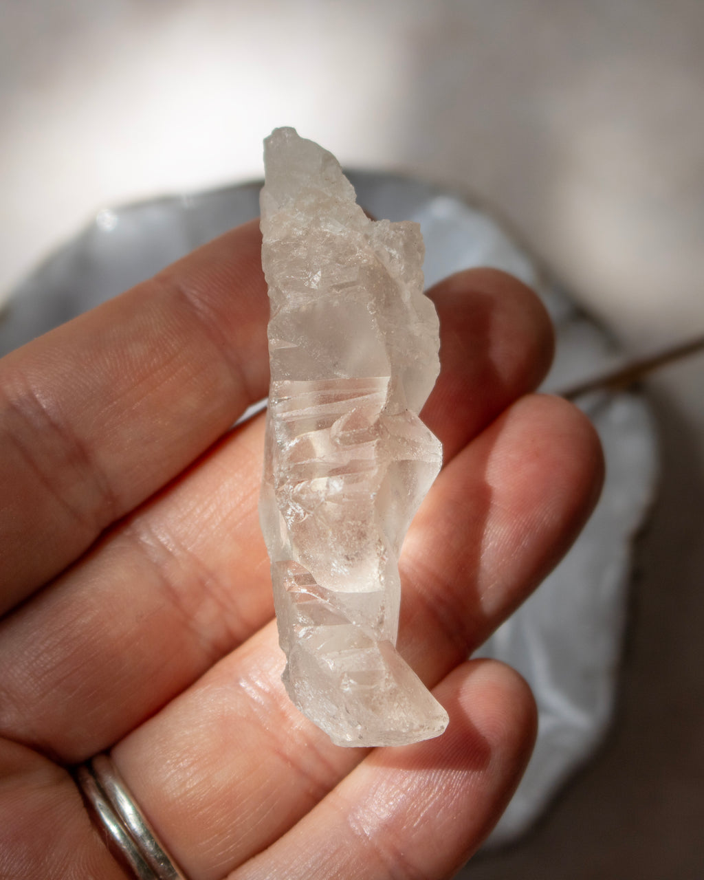 A hand holding a raw, rough translucent white crystal or stone against a softly blurred light gray background.