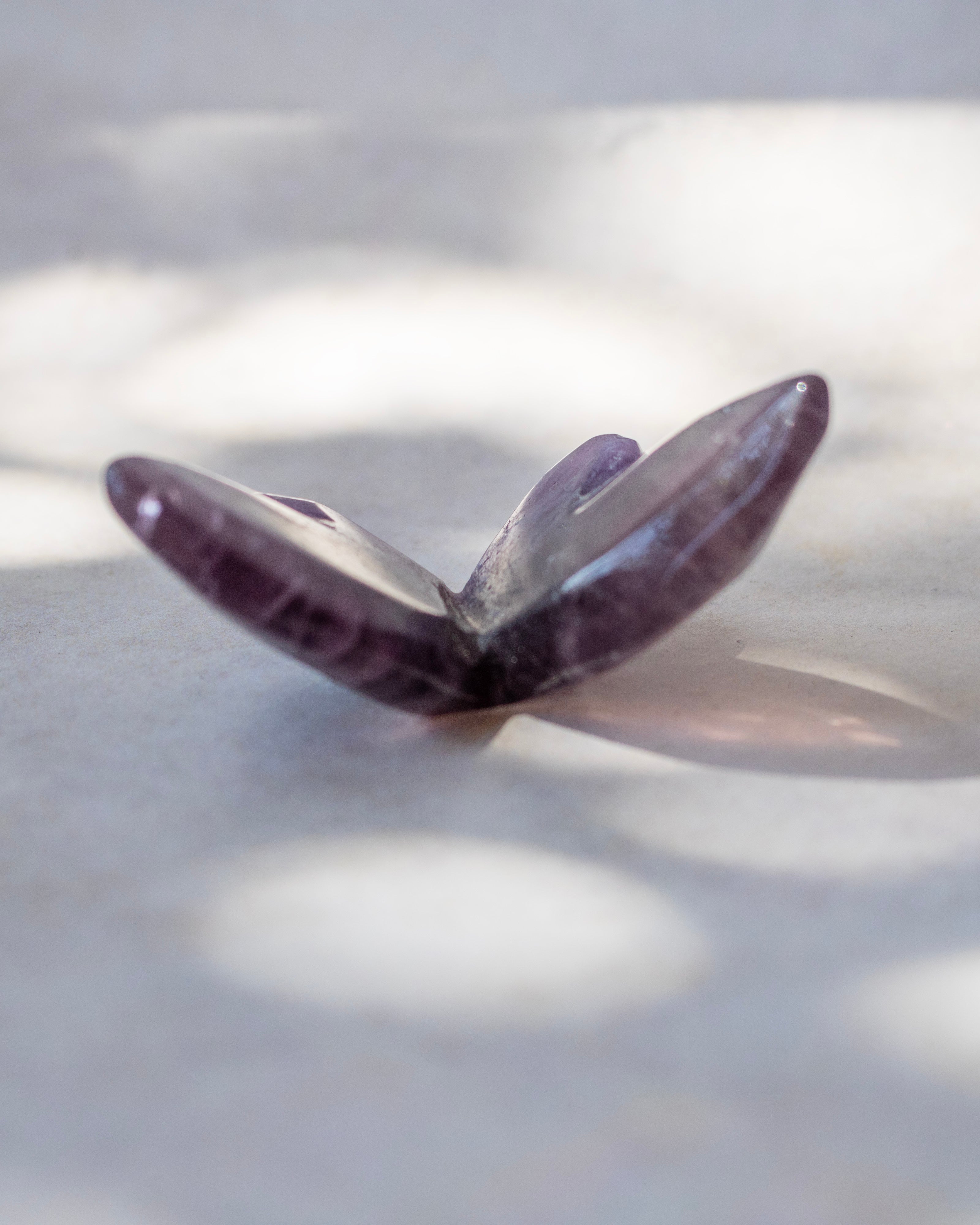 A polished purple crystal butterfly sculpture resting on a light gray surface with soft dappled shadows.