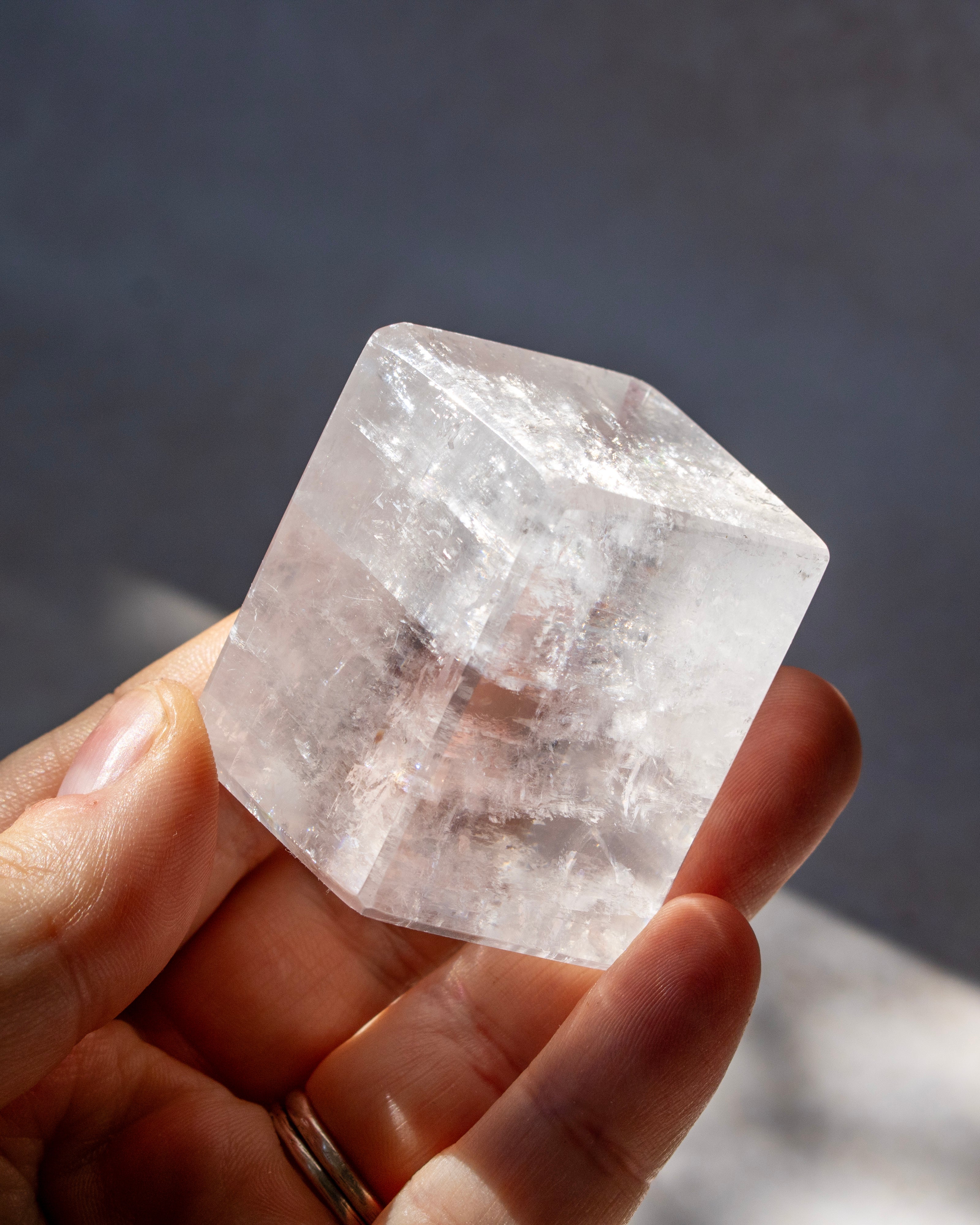 A hand holding a large, translucent clear crystal with natural internal structures and facets, set against a dark gray background.