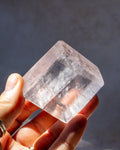 A hand holding a clear, faceted crystal point against a dark gray background.