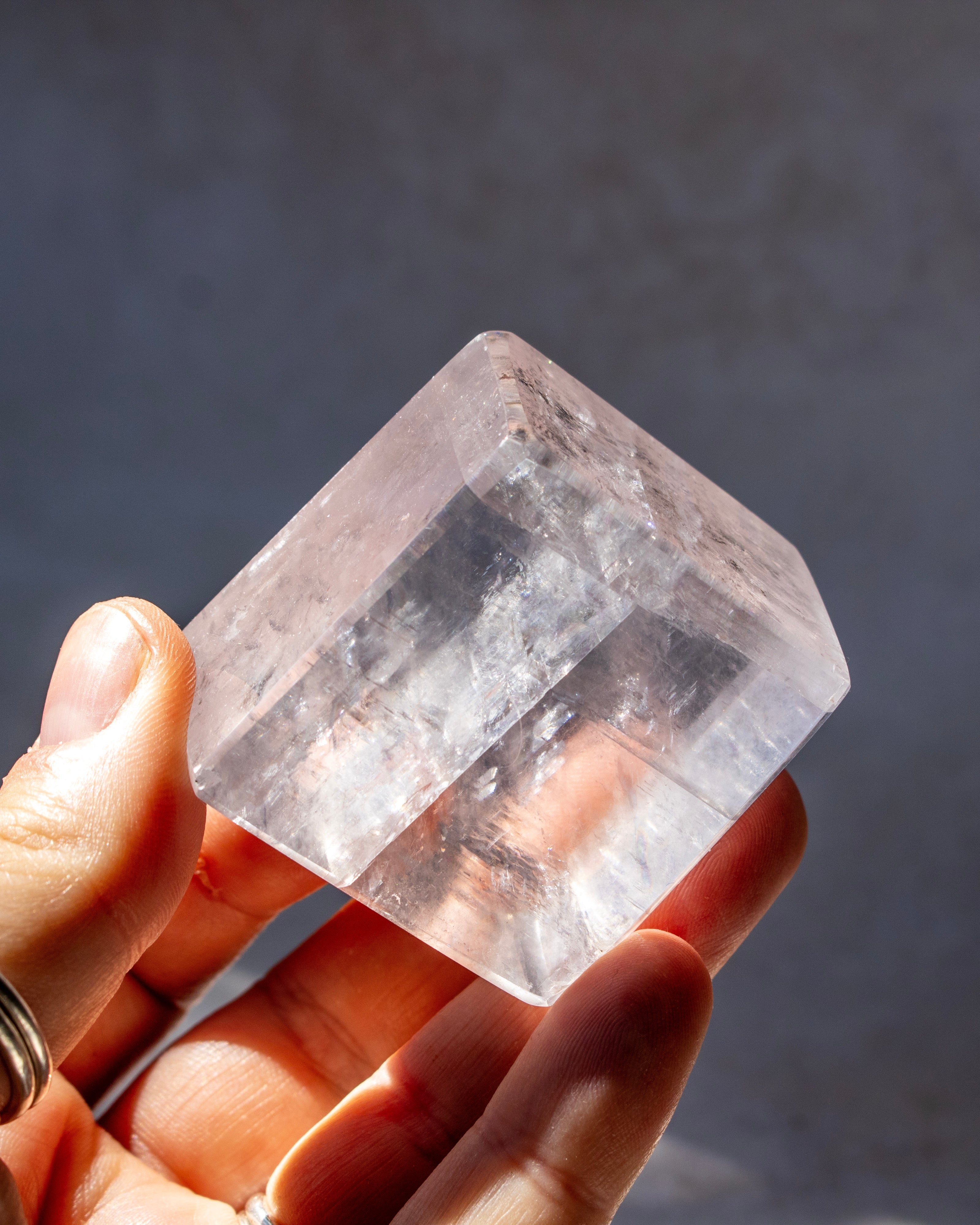 A hand holding a clear, faceted crystal point against a dark gray background.