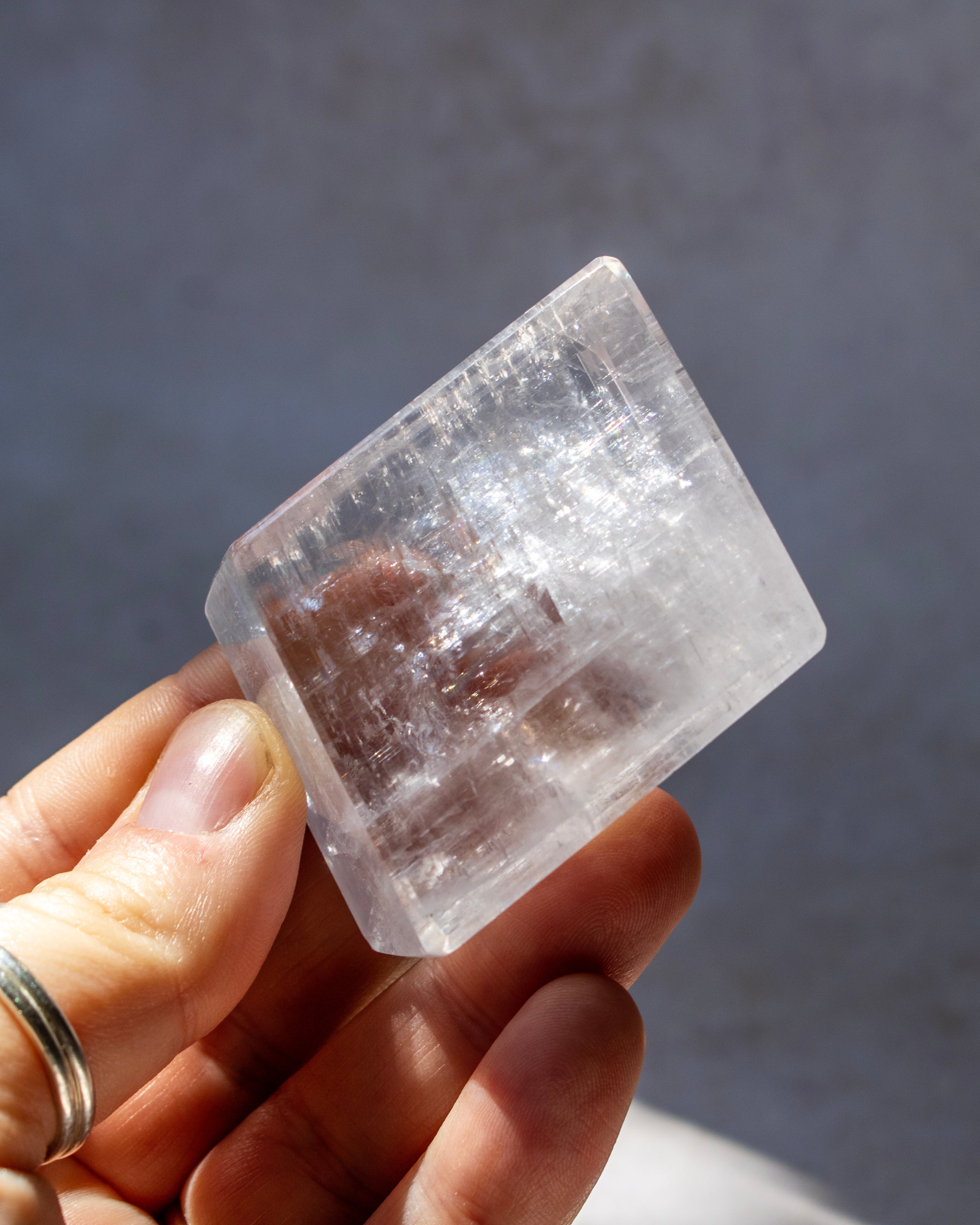 A hand holding a clear, geometric crystal or stone with visible internal striations against a soft gray background.
