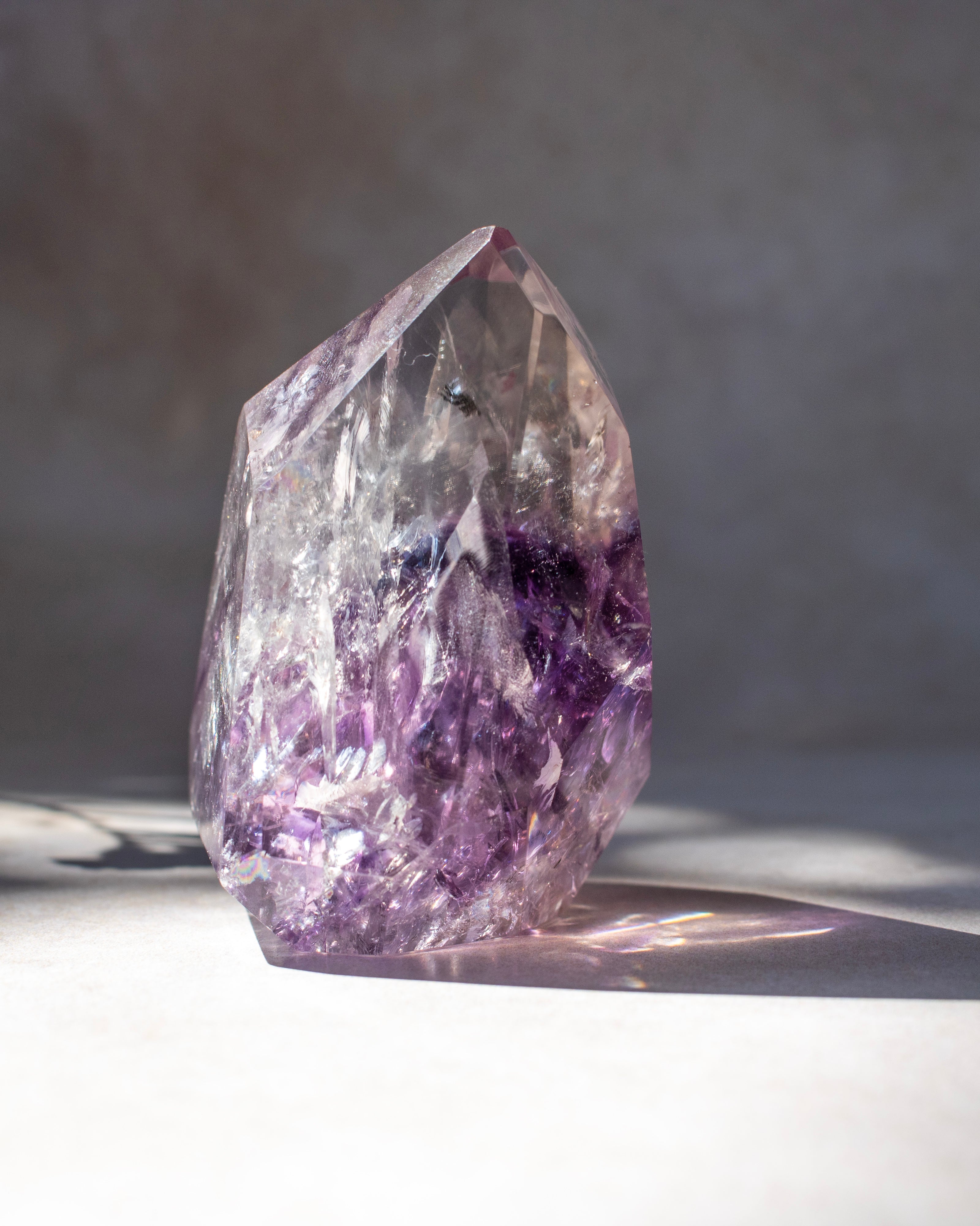 A natural amethyst crystal point with a gradient from clear to deep purple, standing on a light surface with soft shadows.