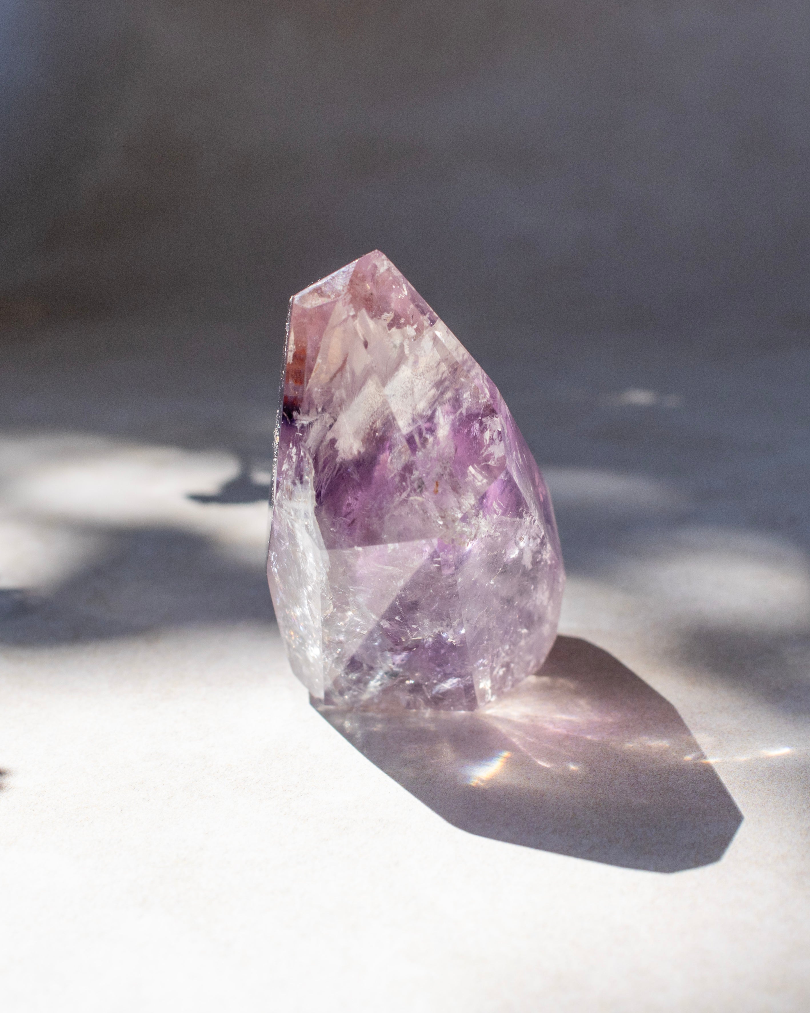 A natural amethyst crystal point with purple and white inclusions, standing on a light surface with dramatic sunlight and shadows.