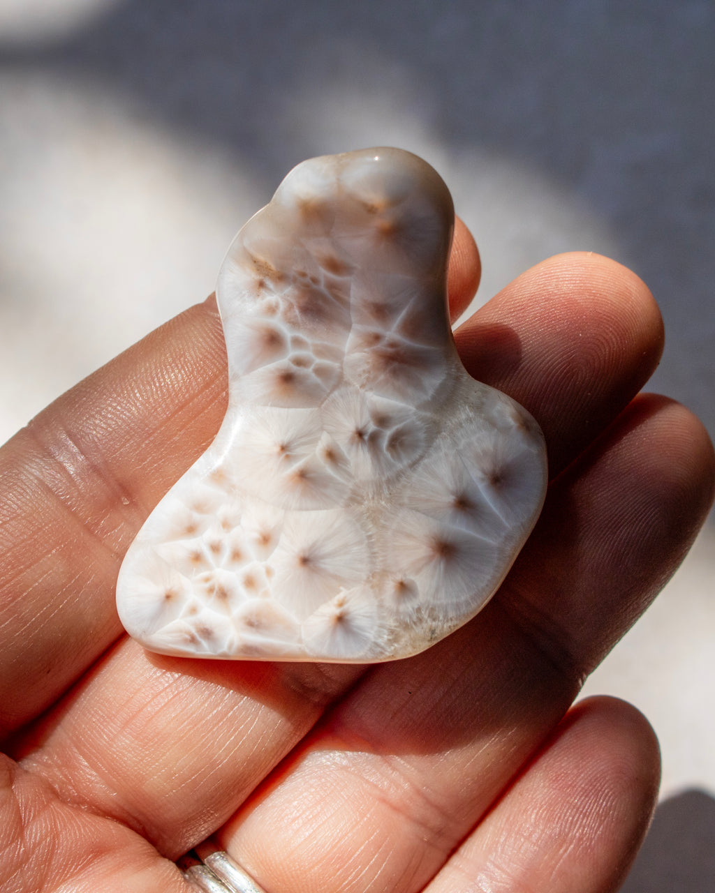 A hand holding a polished carved stone pendant with a natural organic shape, featuring a pattern of small raised nodules on a translucent off-white background.
