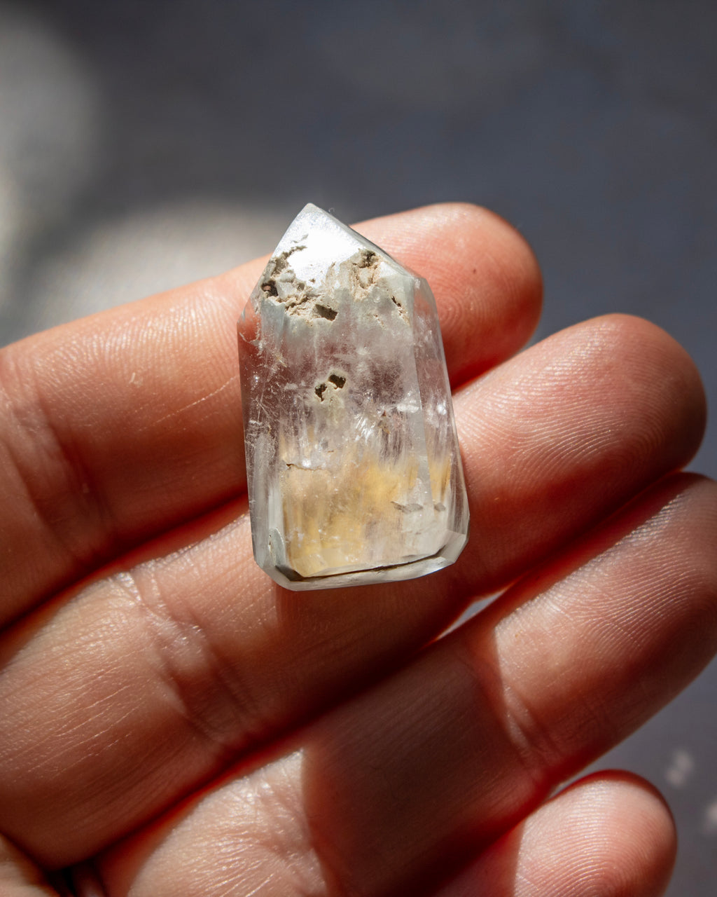 A hand holding a small, natural clear quartz crystal point with visible inclusions and a yellowish tint near the base.