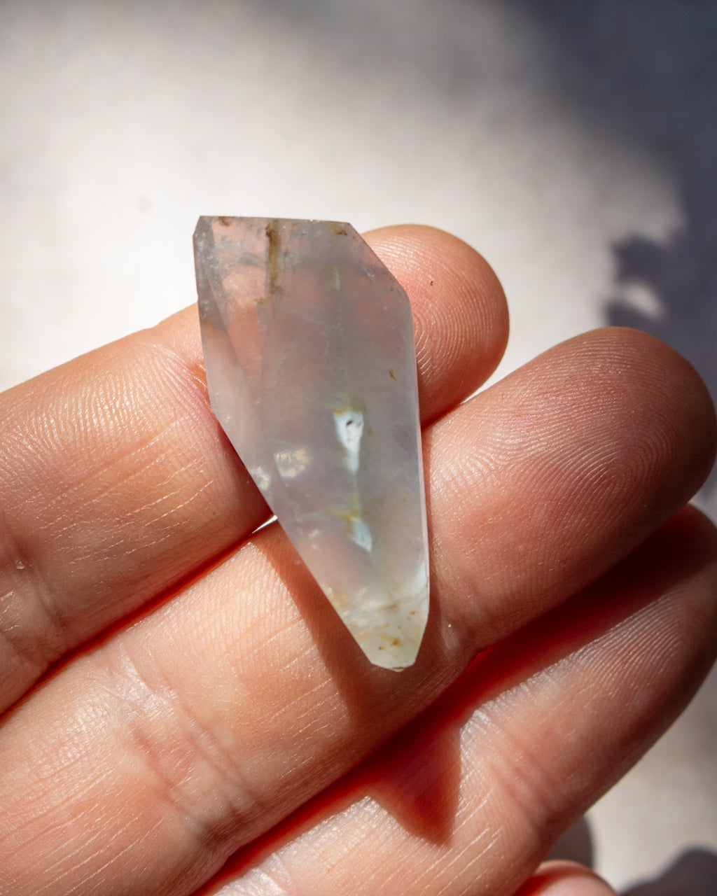 A pointed clear quartz crystal with natural inclusions, held between a person's fingers to show its shape and translucency.