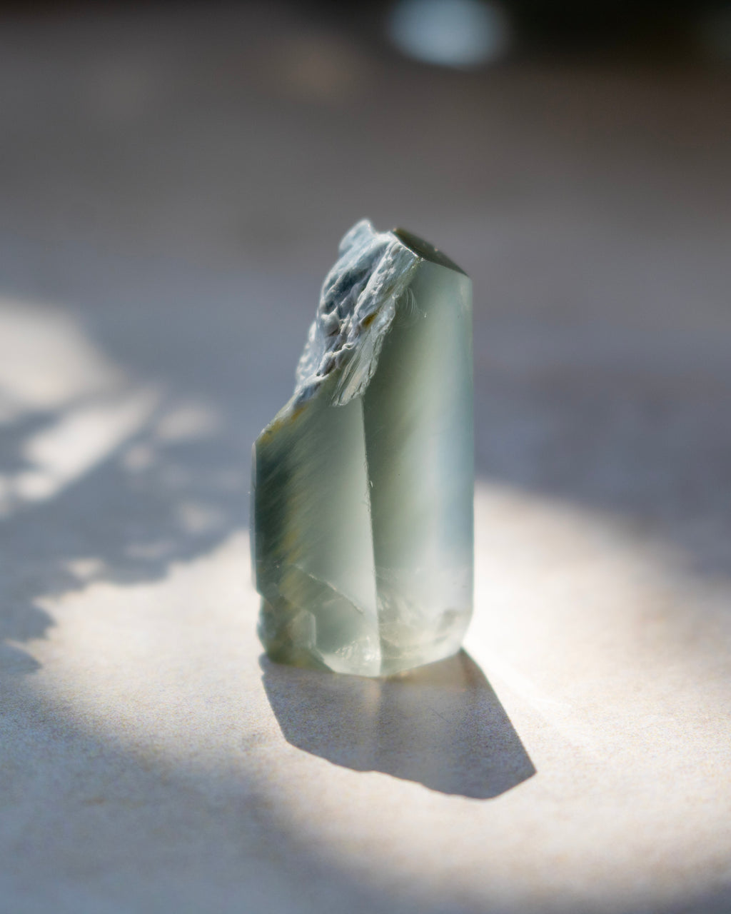 A natural pointed crystal stone with translucent milky white and warm brown inclusions, standing upright on a light surface under direct sunlight with a soft shadow.