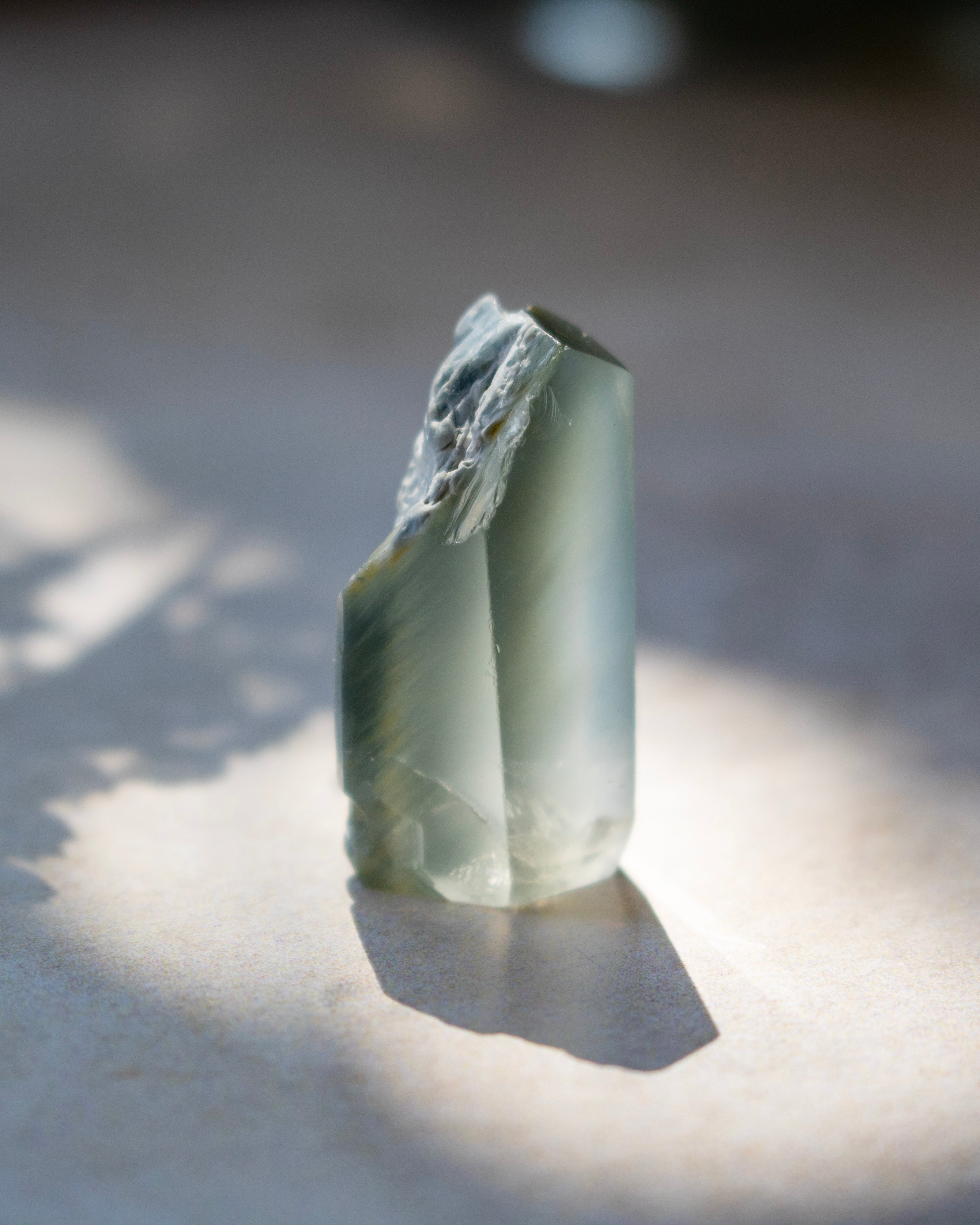 A natural pointed crystal stone with translucent milky white and warm brown inclusions, standing upright on a light surface under direct sunlight with a soft shadow.