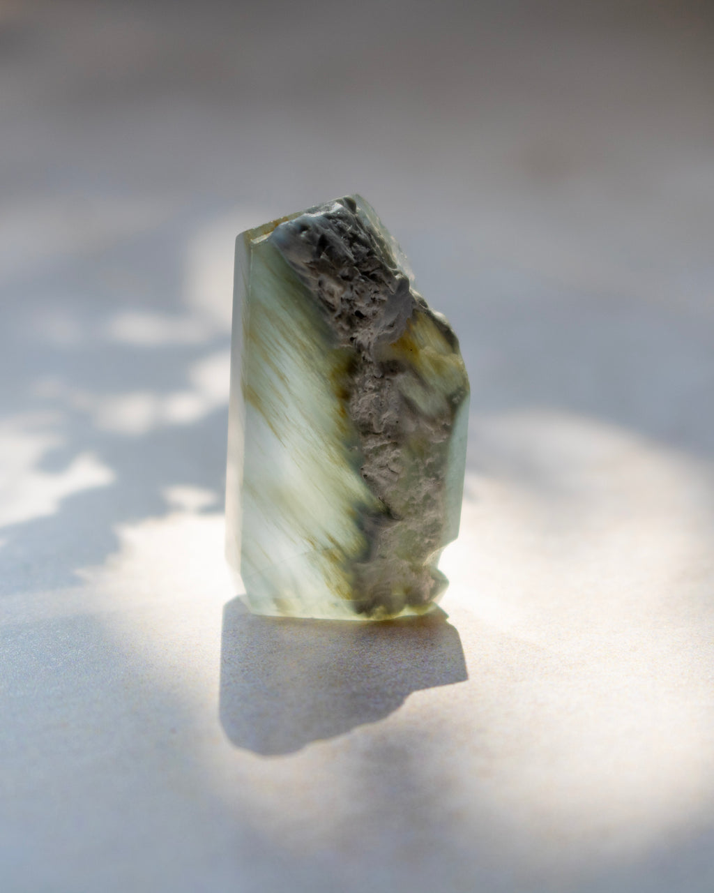 A natural pointed crystal stone with translucent milky white and warm brown inclusions, standing upright on a light surface under direct sunlight with a soft shadow.