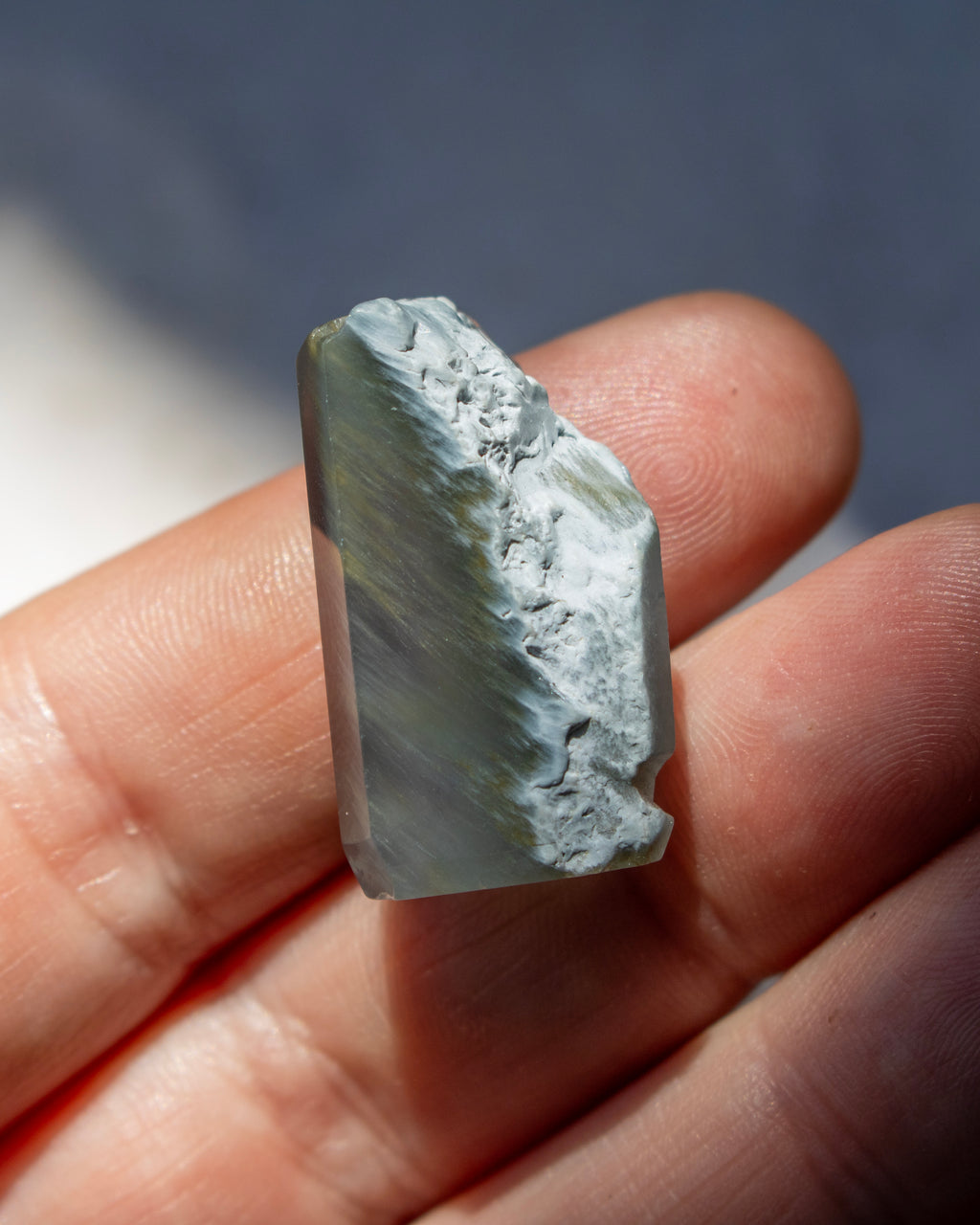A natural pointed crystal stone with translucent milky white and warm brown inclusions, being held under direct sunlight with a soft shadow.
