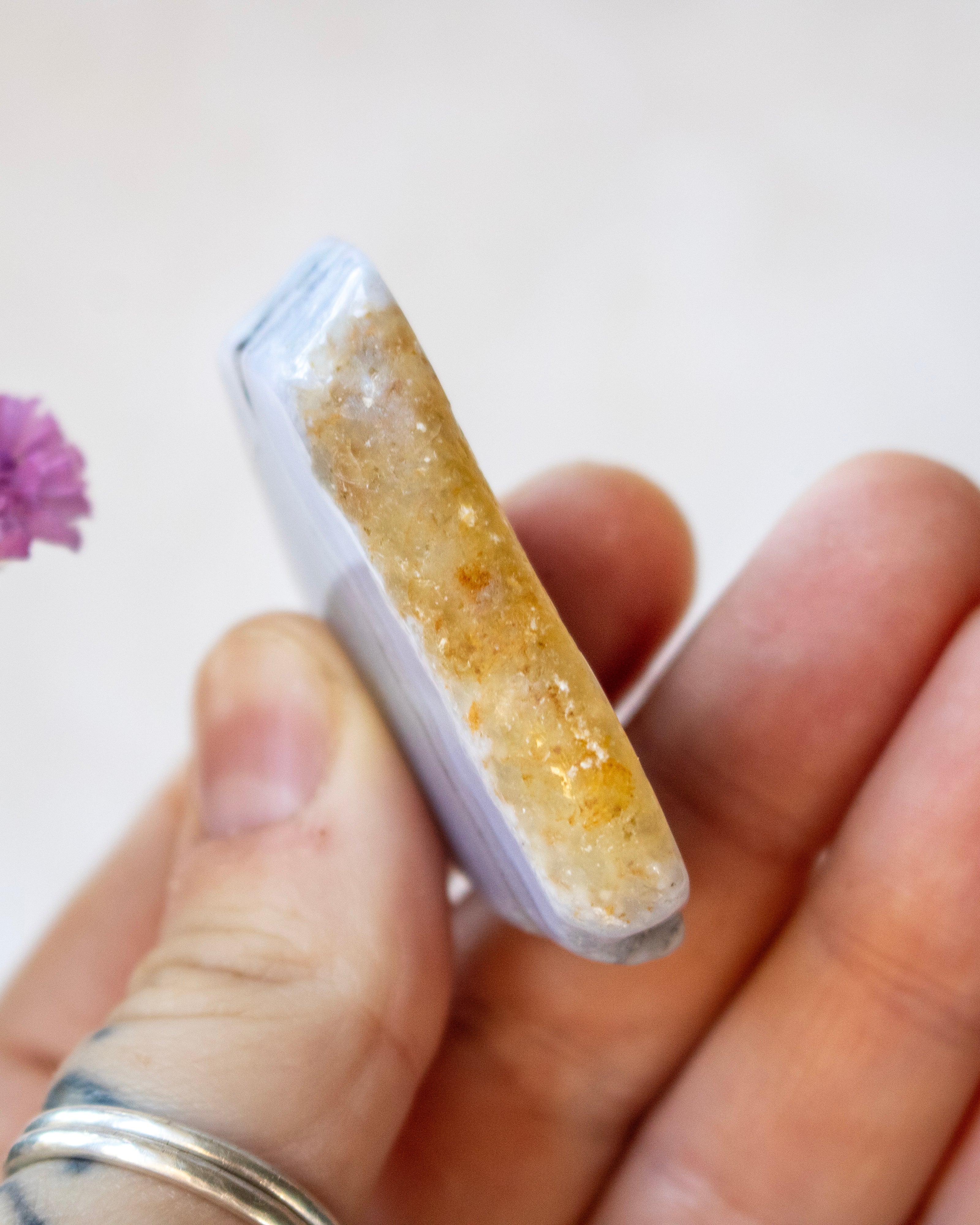 A hand holding a polished crystal cluster with a pale lavender outer layer and a golden-yellow crystalline core, shown close-up against a soft light background.