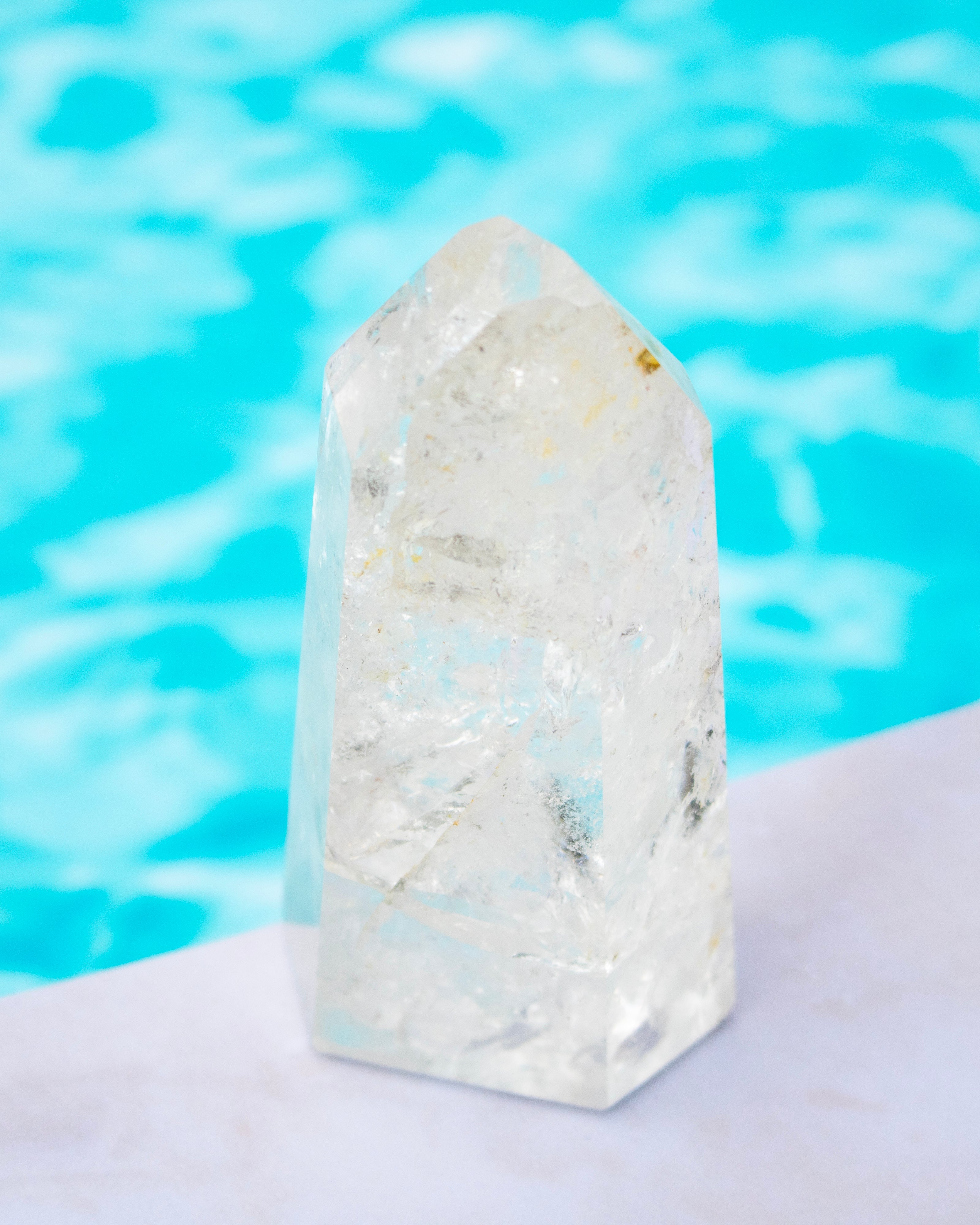 A clear quartz crystal point tower standing on a white surface with a bright blue swimming pool in the background.