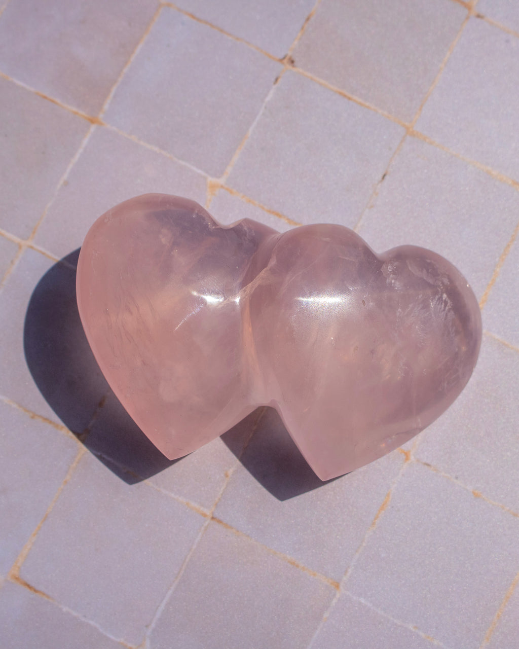 A translucent pink heart-shaped crystal sculpture resting on a light gray tiled surface.