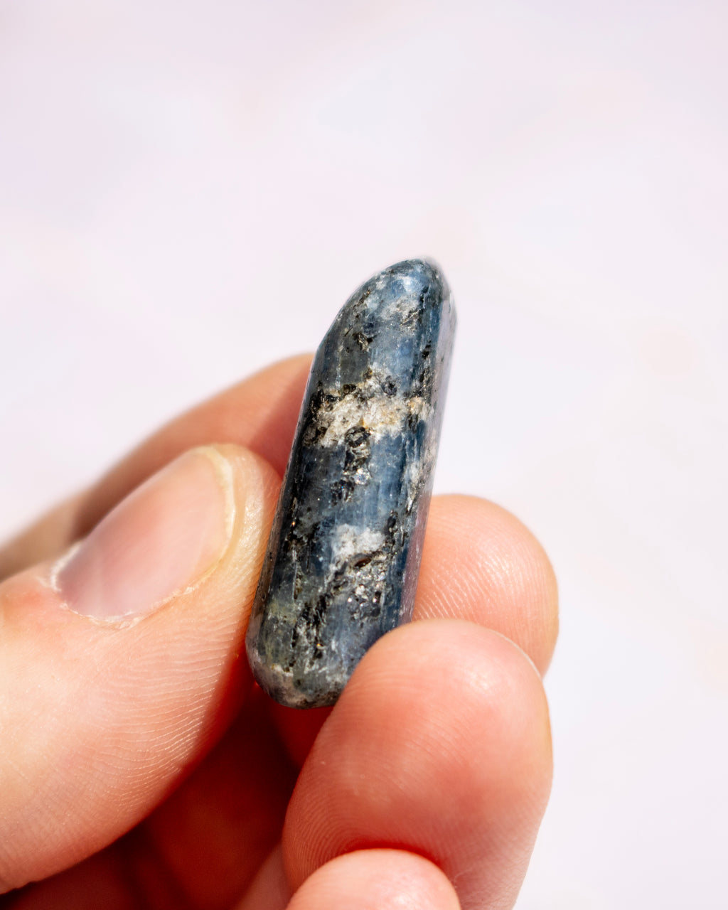 A hand holding a polished blue-gray stone with natural white and dark inclusions against a soft light background.