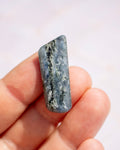 A hand holding a polished rectangular blue-gray stone with natural white and dark veining, shown close-up against a soft light background.