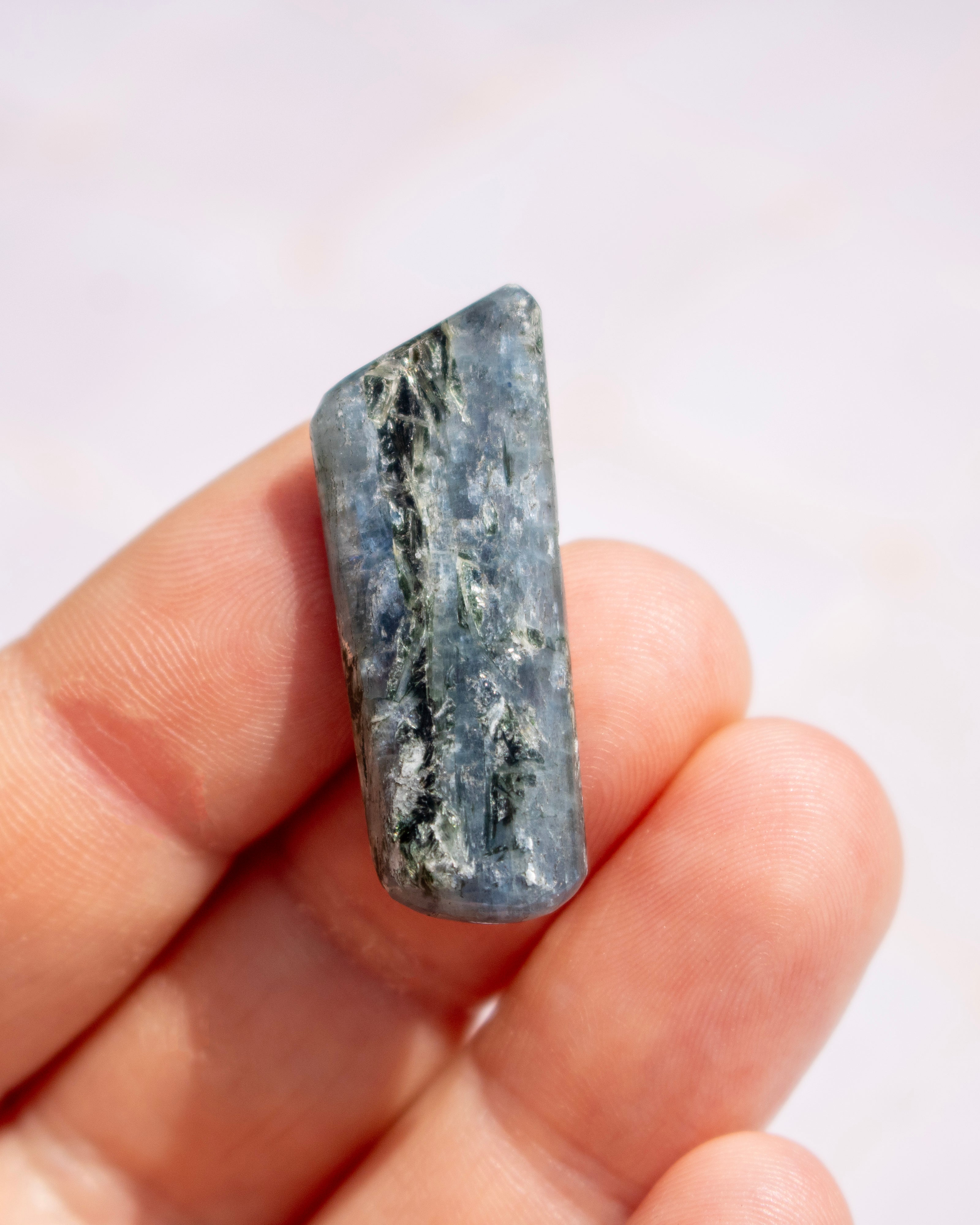 A hand holding a polished rectangular blue-gray stone with natural white and dark veining, shown close-up against a soft light background.