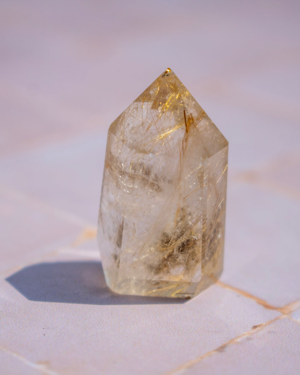 A natural pointed crystal tower with internal golden inclusions, standing on a light marble surface.
