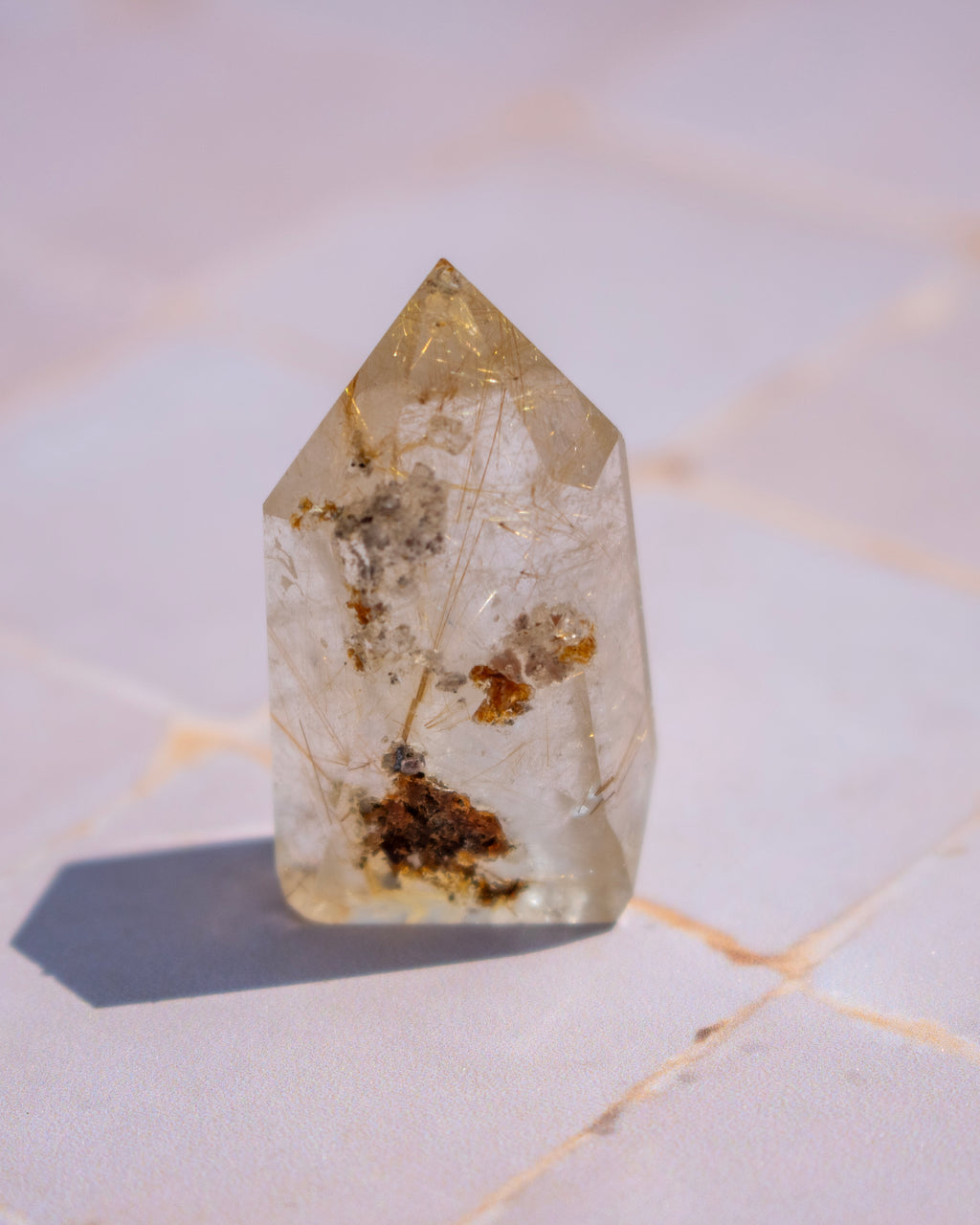 A pointed clear quartz crystal point with internal inclusions and brownish deposits, standing on a light stone surface.