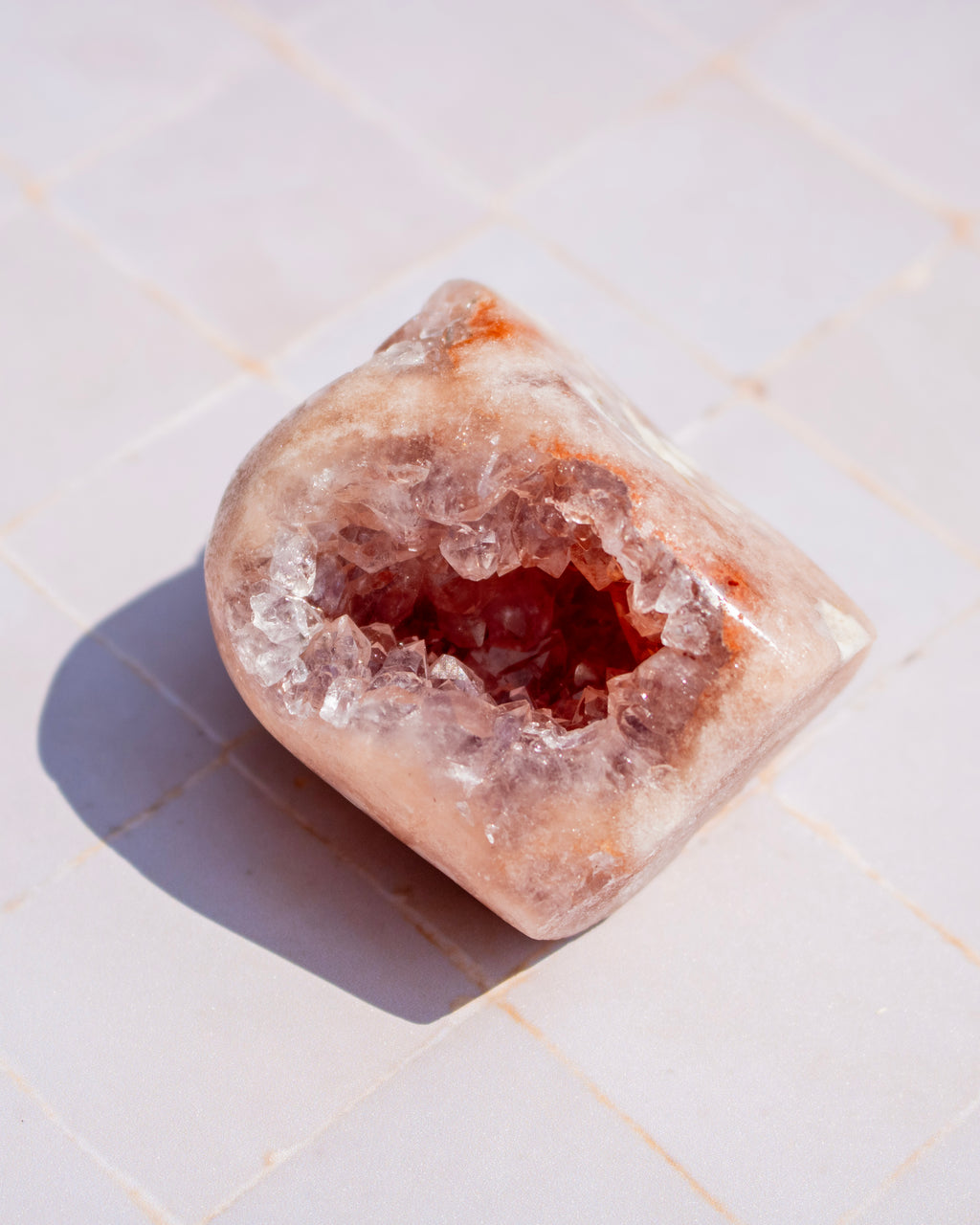 A polished rose quartz crystal geode with a hollowed-out interior, resting on a light beige tiled surface.