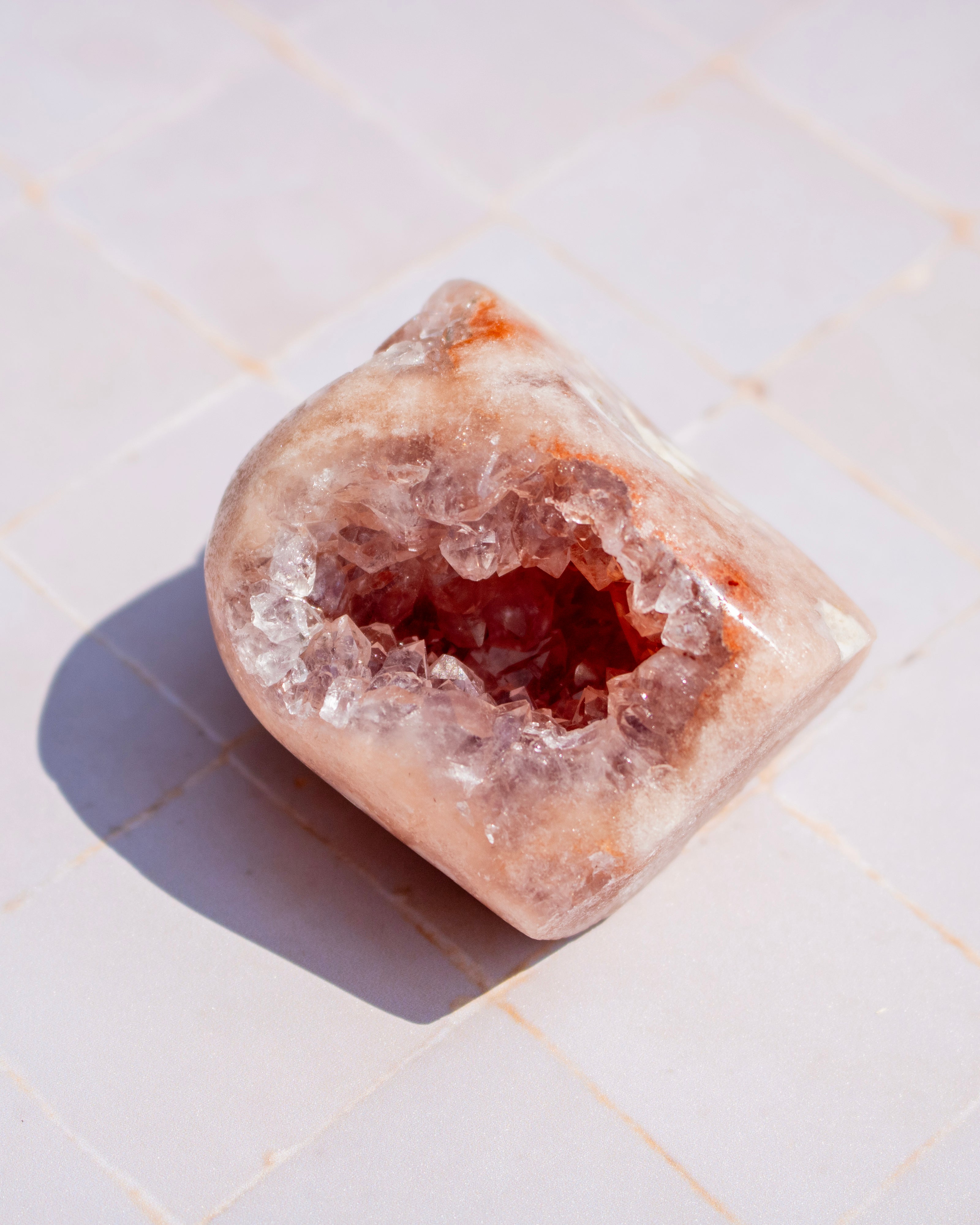 A polished rose quartz crystal geode with a hollowed-out interior, resting on a light beige tiled surface.
