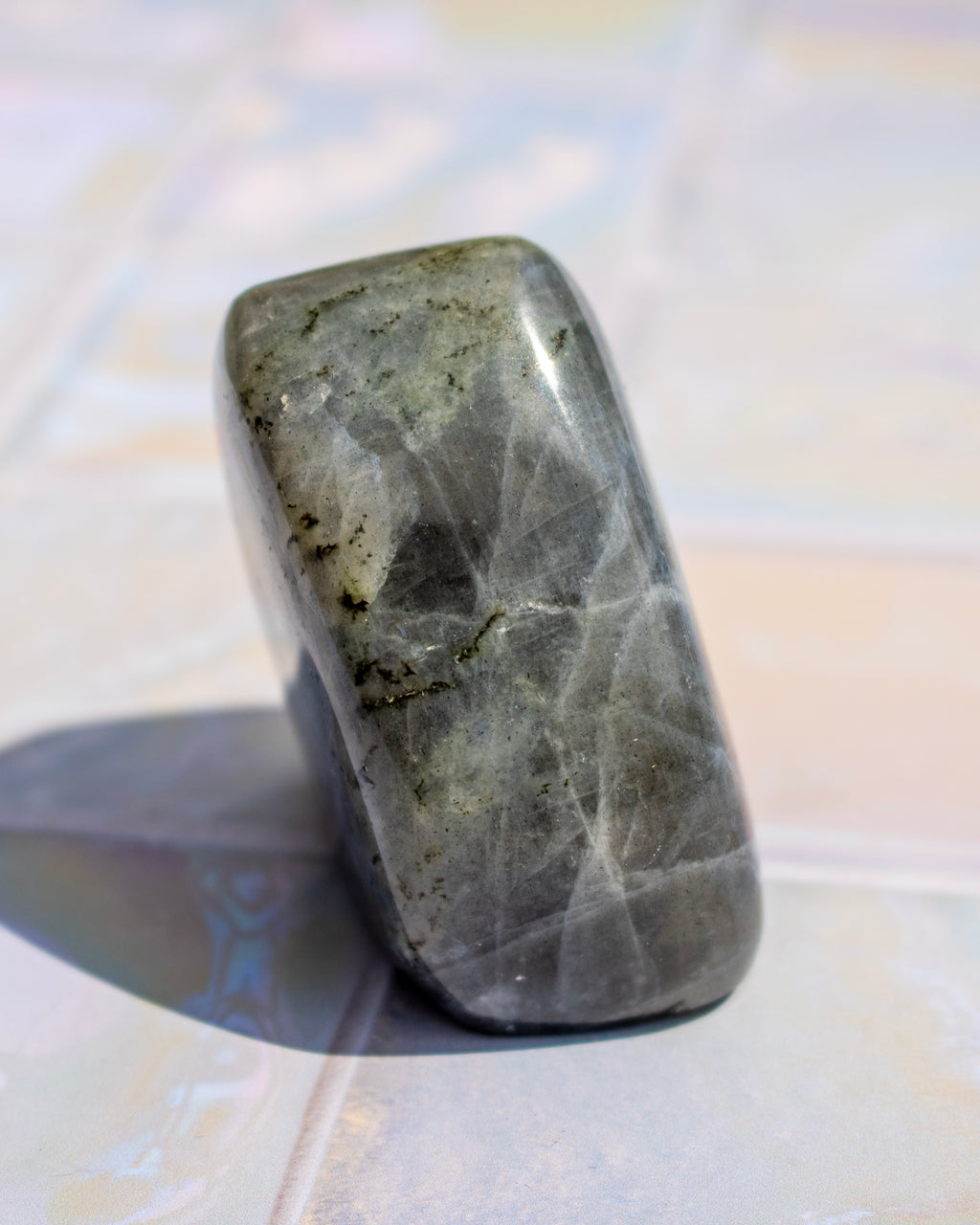 A polished gray stone tumbled into a rounded rectangular shape, standing upright on a light tiled surface with a soft shadow to the left.
