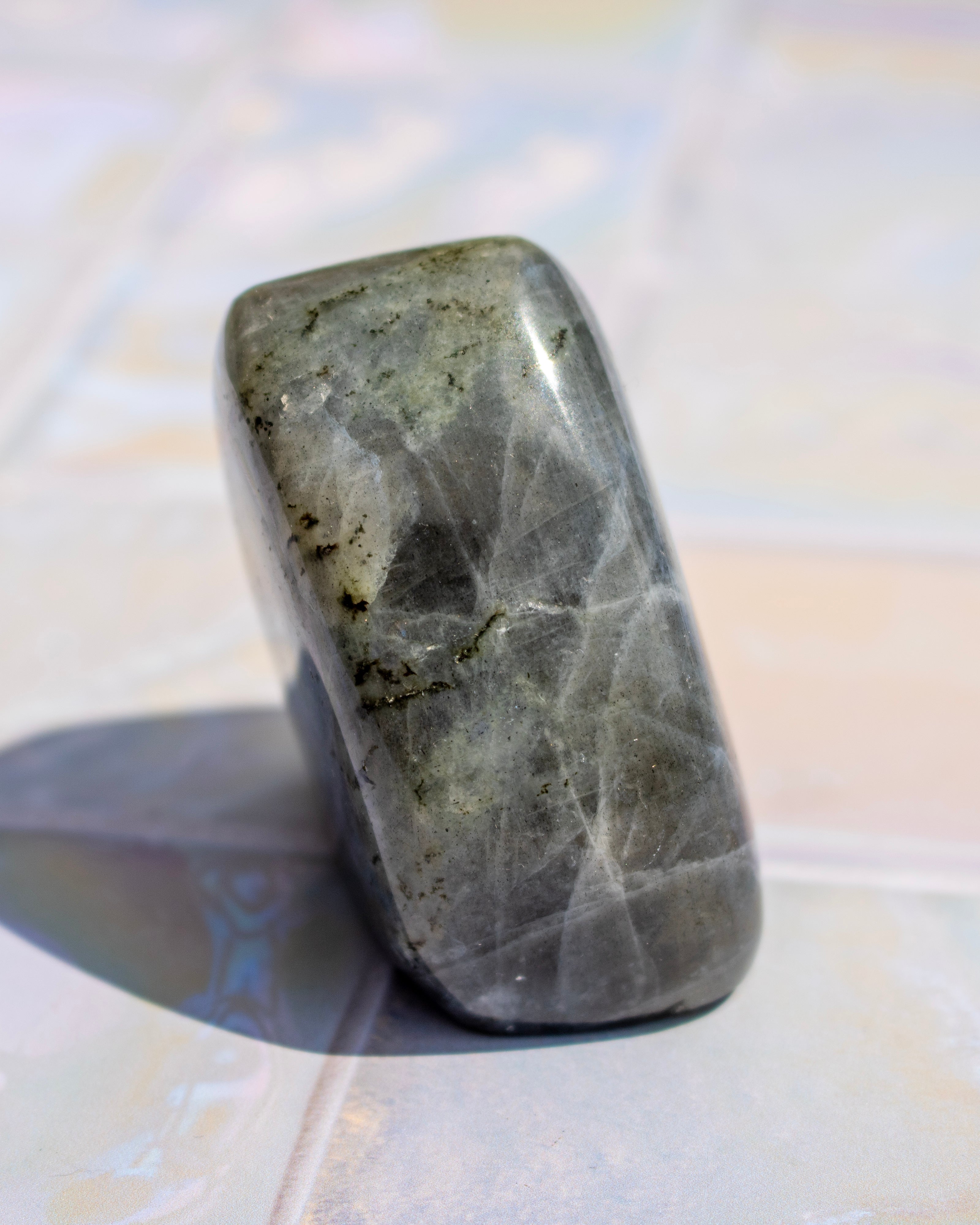 A polished gray stone tumbled into a rounded rectangular shape, standing upright on a light tiled surface with a soft shadow to the left.
