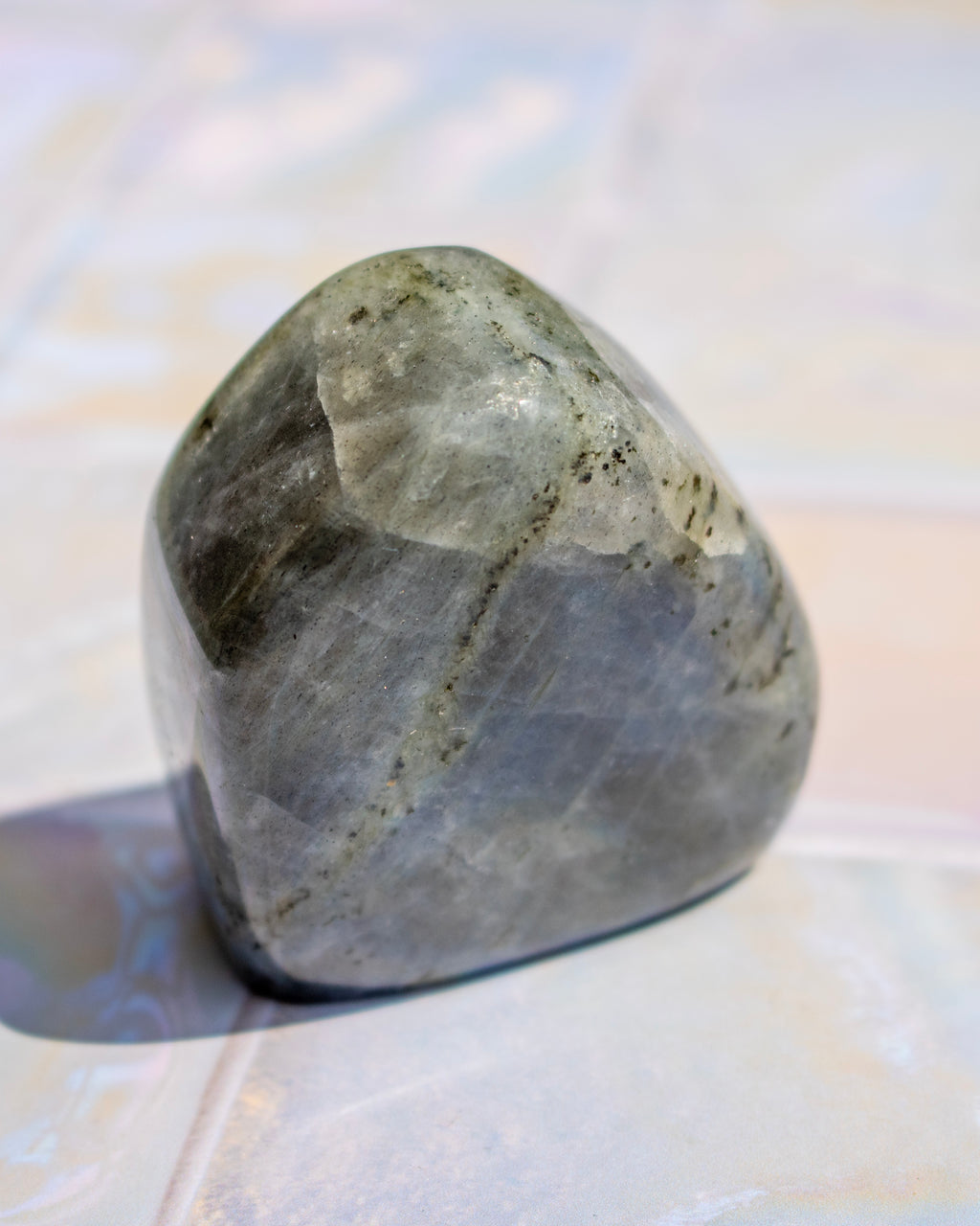 A polished gray stone with natural dark veining and a smooth, rounded surface, photographed on a light marble-like surface.