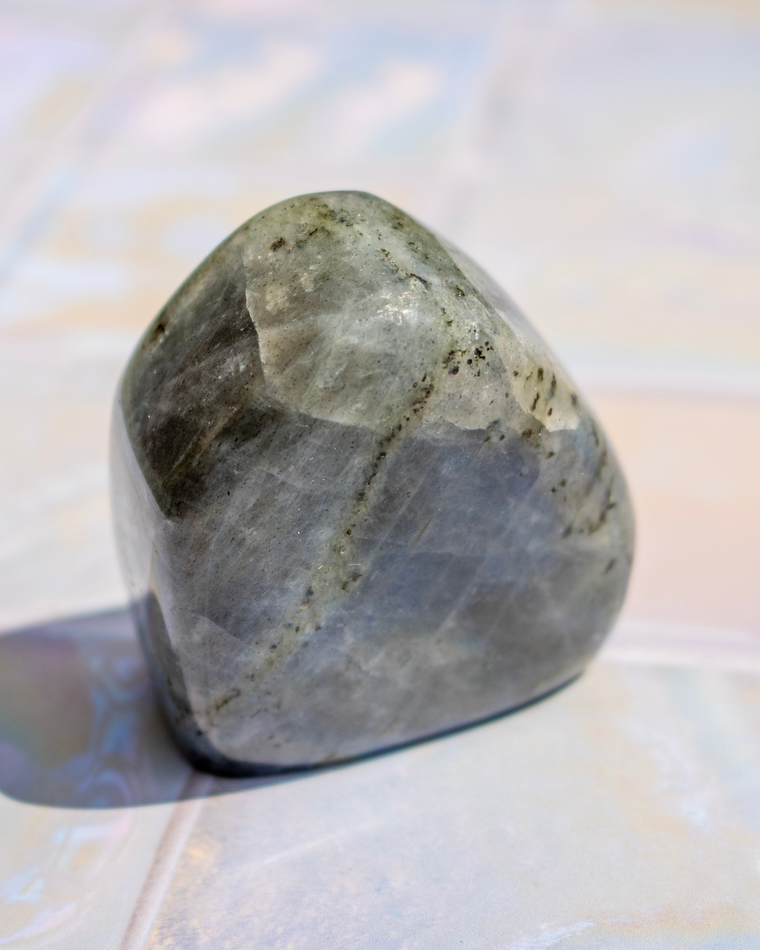 A polished gray stone with natural dark veining and a smooth, rounded surface, photographed on a light marble-like surface.