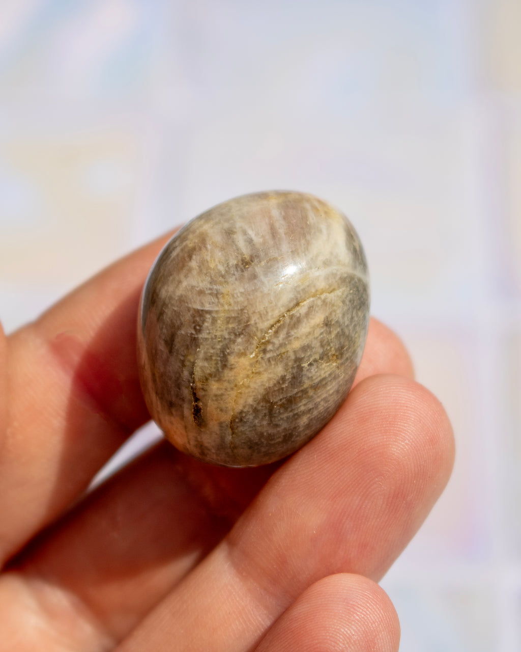 A hand holding a polished, oval-shaped stone with natural beige, brown, and gray marbled patterns.