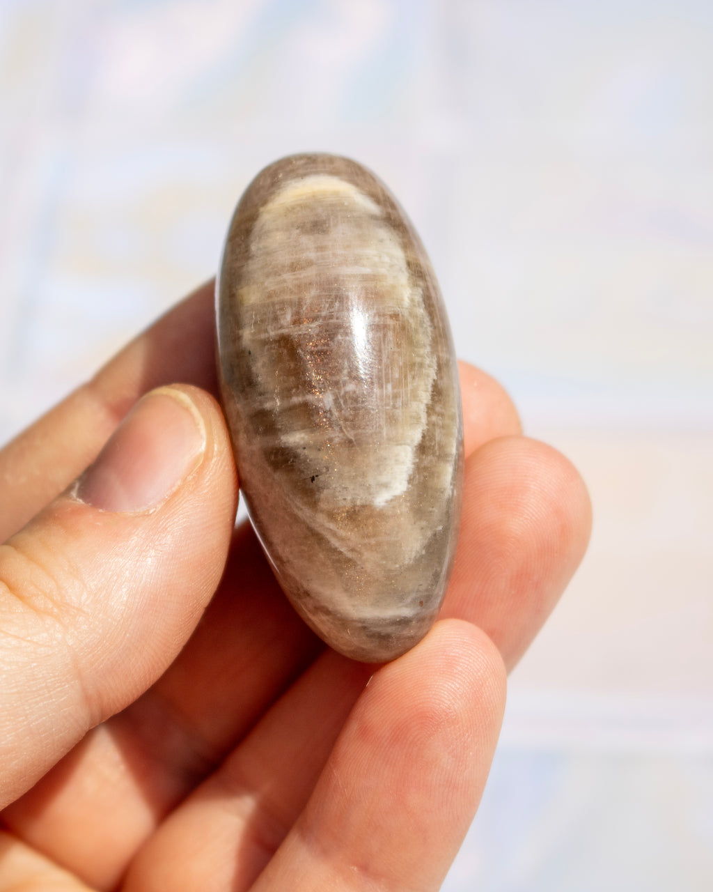 A hand holding a polished, oval-shaped brown stone with natural banding and a smooth, glossy finish.