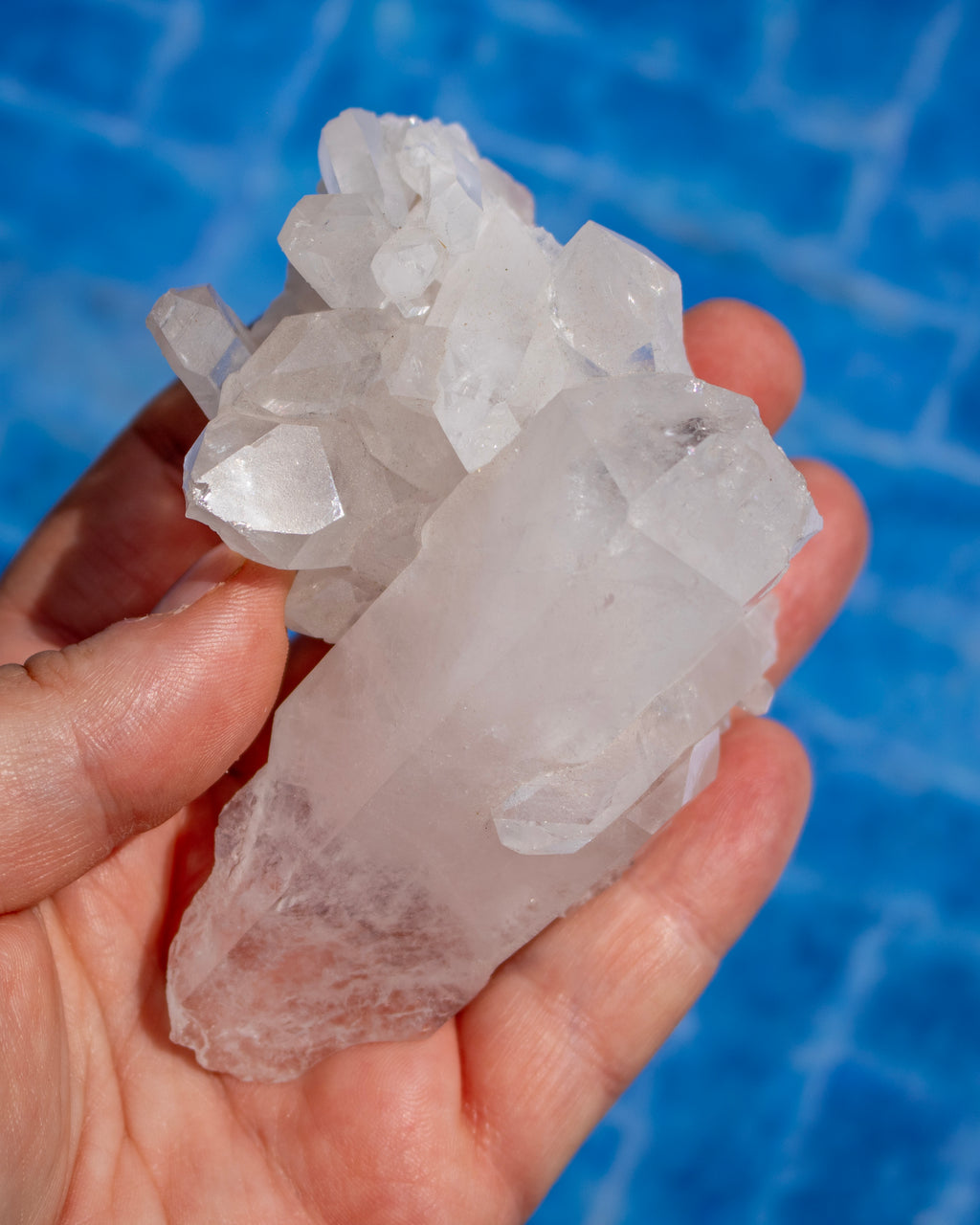 A hand holding a cluster of translucent white crystals, with a bright blue tiled background.