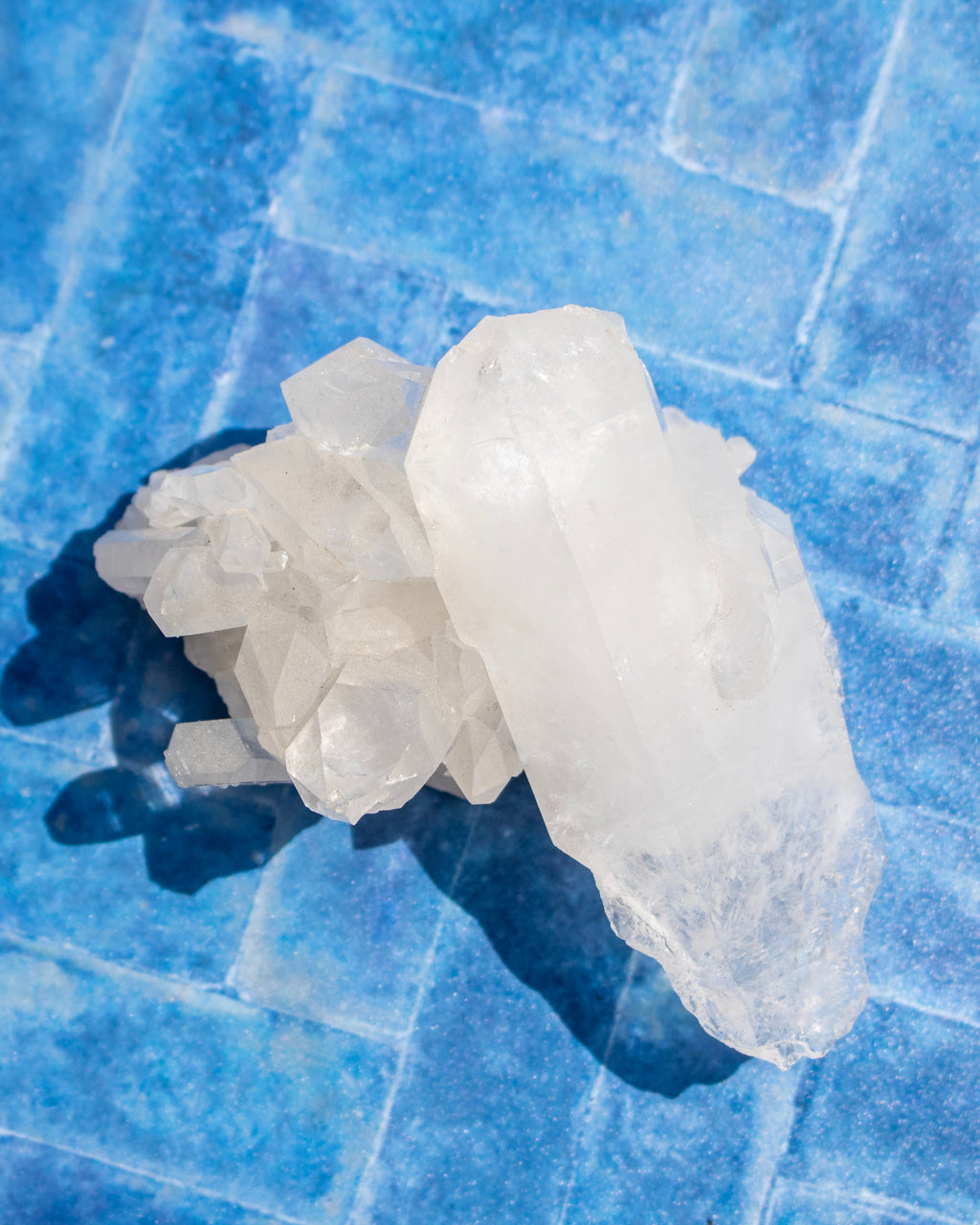 A cluster of translucent white crystals resting on a textured blue tiled surface, casting a dark shadow.