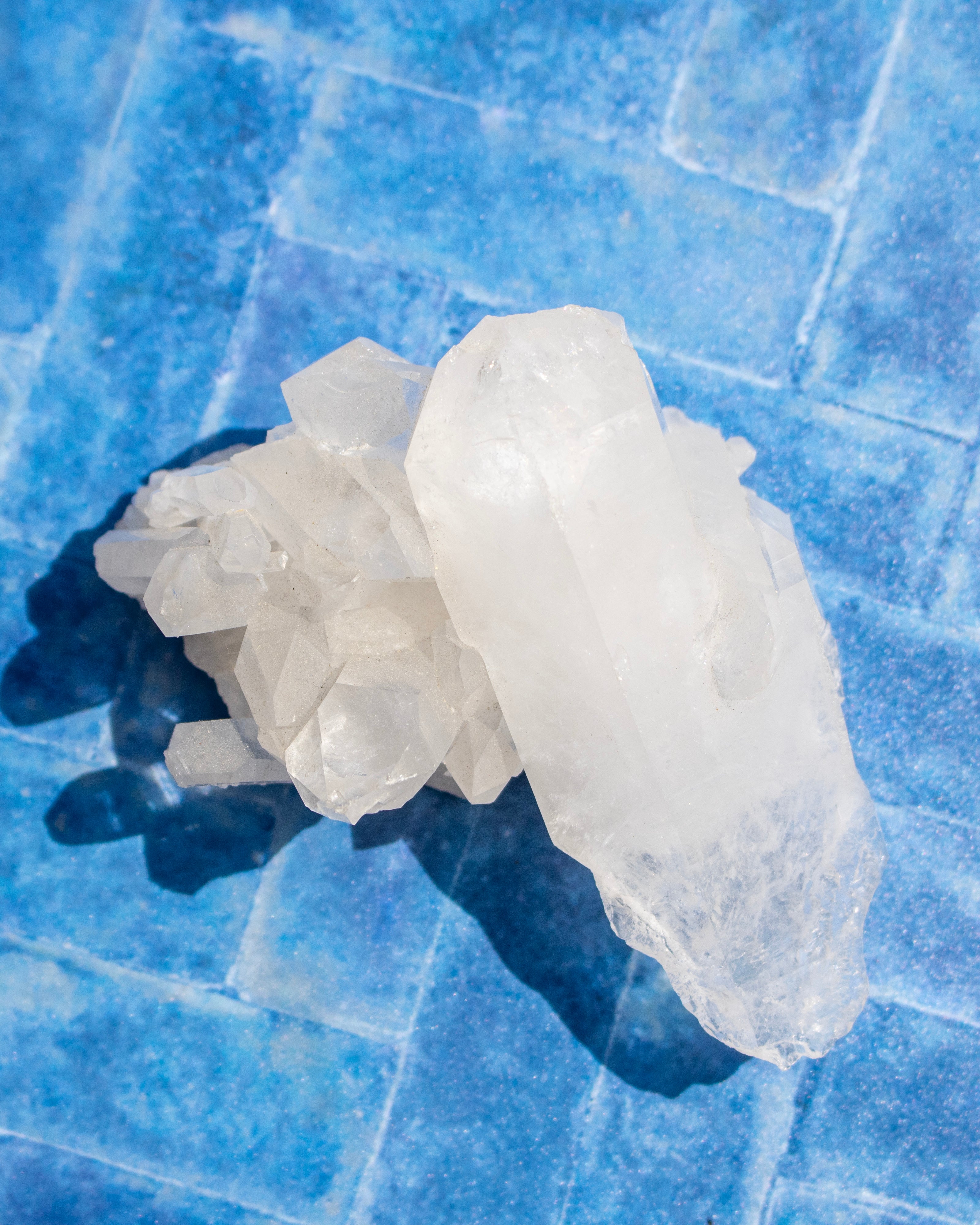 A cluster of translucent white crystals resting on a textured blue tiled surface, casting a dark shadow.