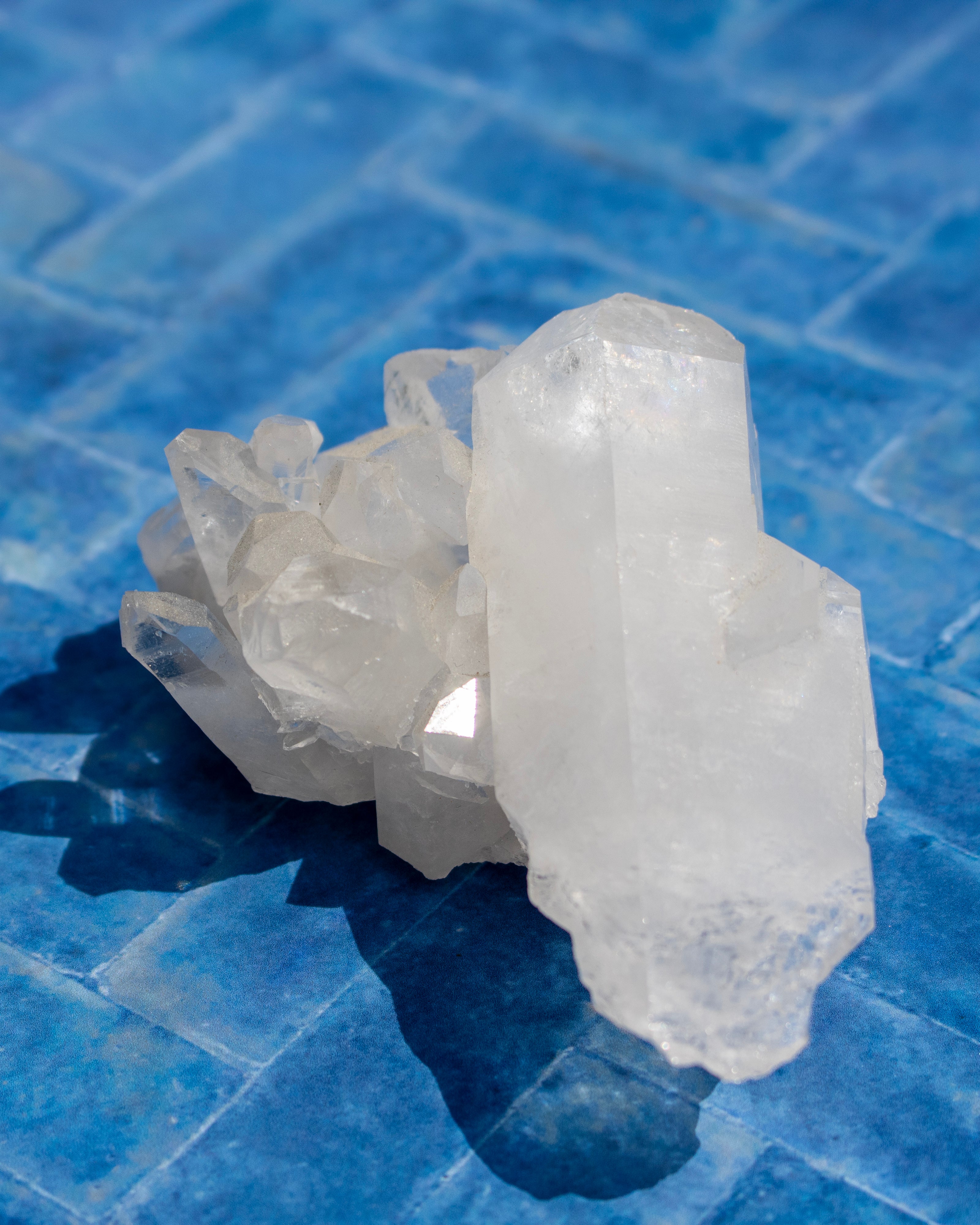 A cluster of natural white quartz crystals with a prominent tall point, resting on a glossy blue tiled surface.
