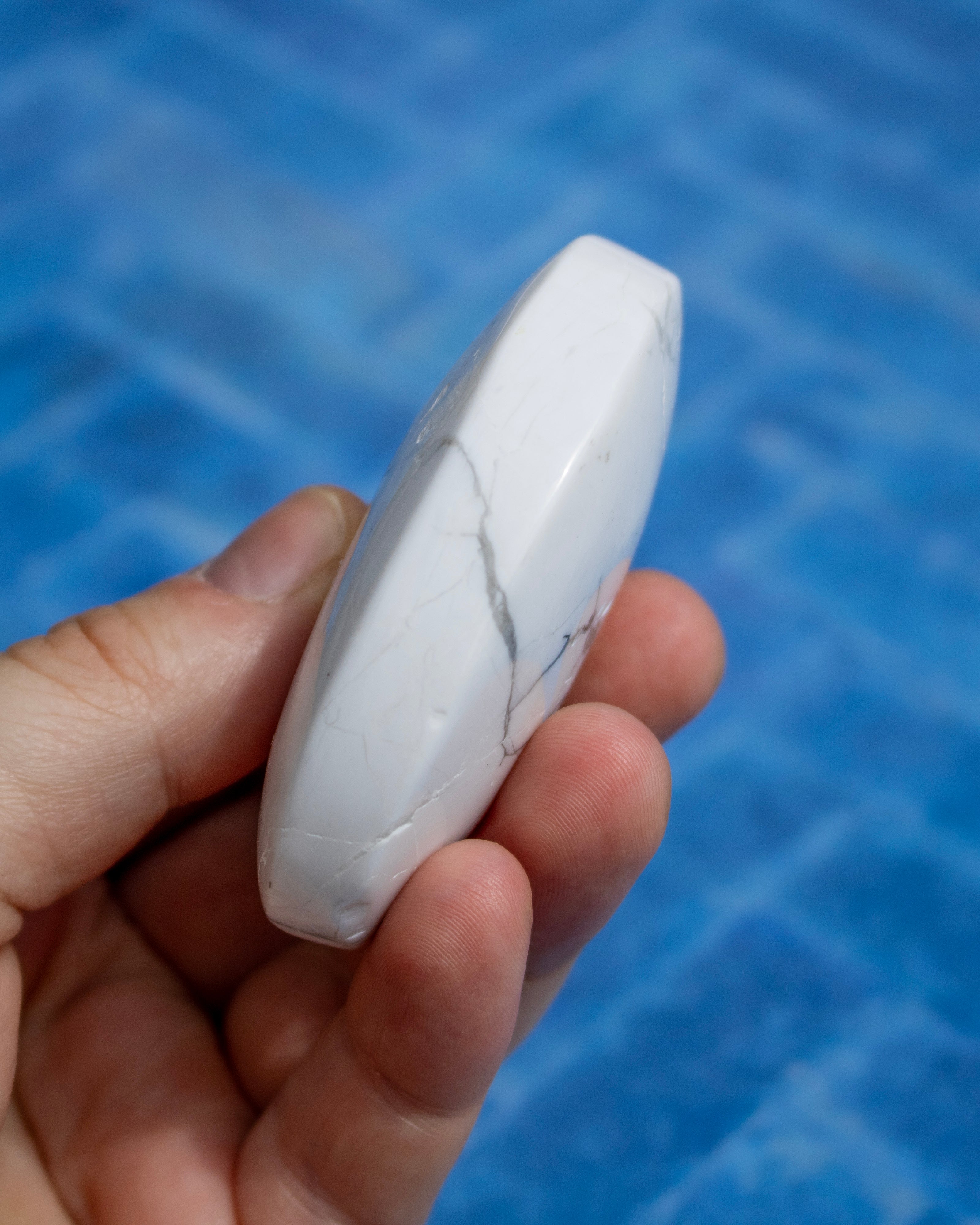 A hand holding a polished white stone or crystal with natural gray veining, set against a textured blue background.