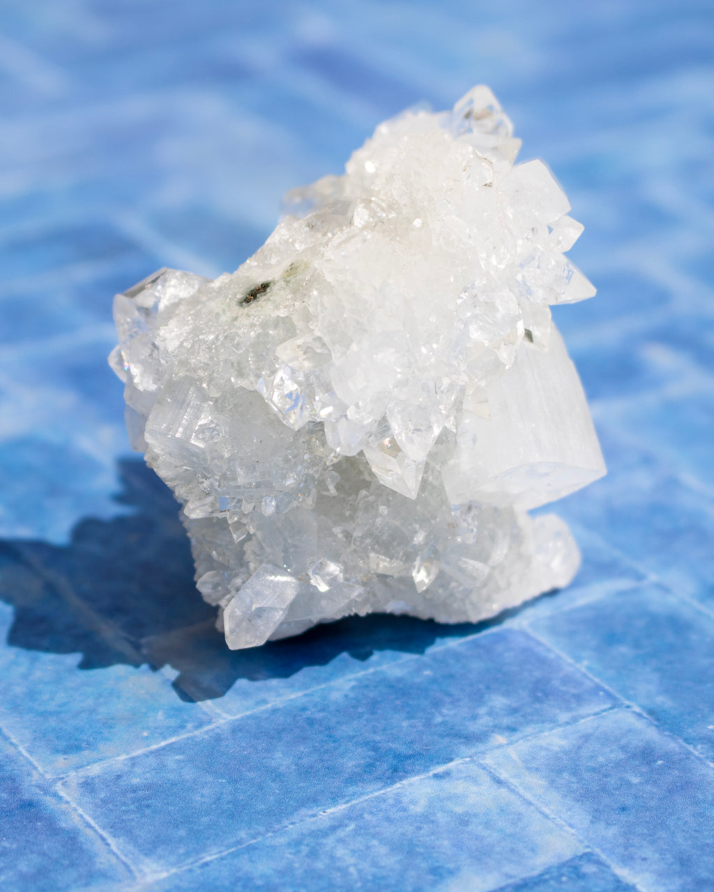 A raw white crystal cluster with sharp faceted mineral points, photographed standing on a blue tiled surface.