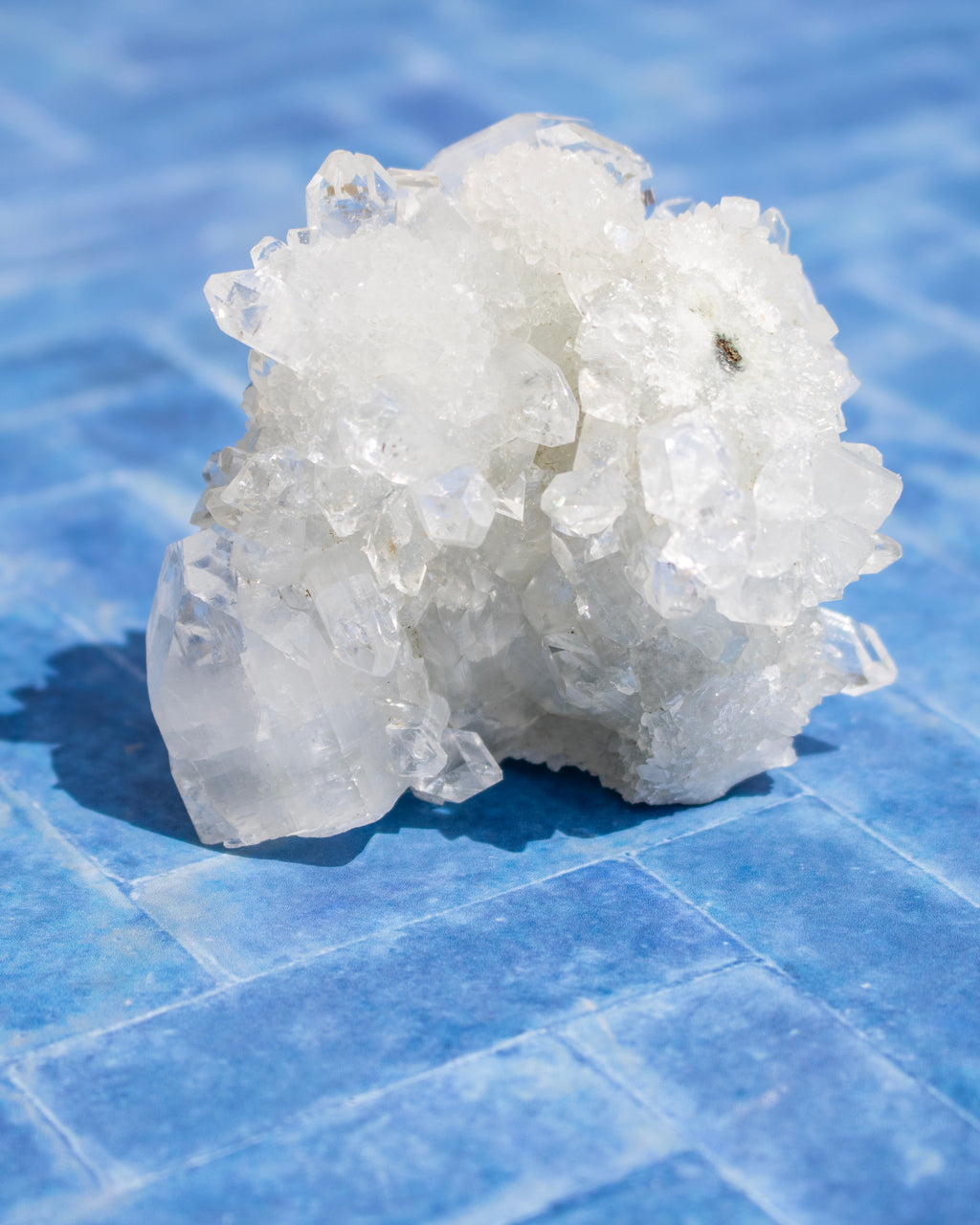 A cluster of translucent white crystals with a rough, natural texture, resting on a blue tiled surface.